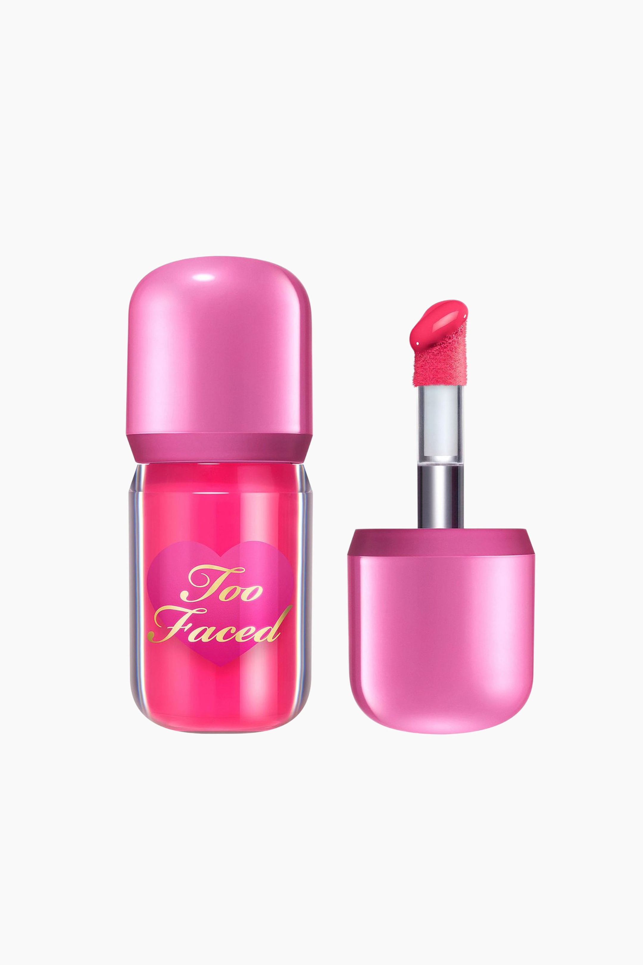 Visa större bild: En Too Faced läppglans presenteras i en klar, cylindrisk flaska fylld med livfullt rosa glans, med en rosa hjärtetikett med guldfärgad 'Too Faced' text, och toppad med en glansig rosa rundad kork. Bredvid står applikatorn upprätt, visar sin ludna, vinklade spets täckt i ljusrosa glans, fäst vid en silverstav och en matchande glansig rosa kork.