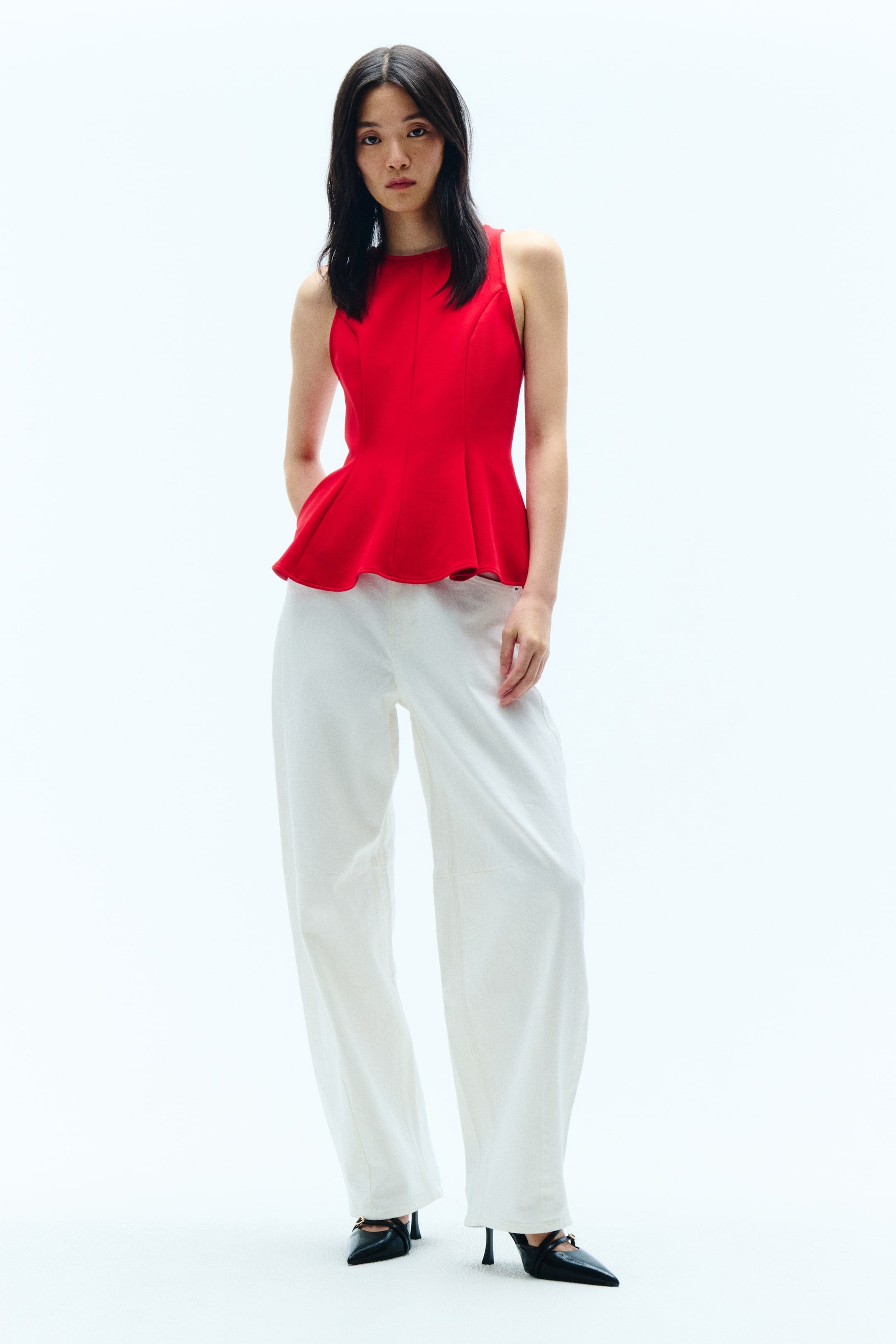 View larger image: A red peplum top, shown from the front, features a round neckline and a sleeveless design. The fitted bodice has vertical seams and flares out at the waist into a peplum hem.