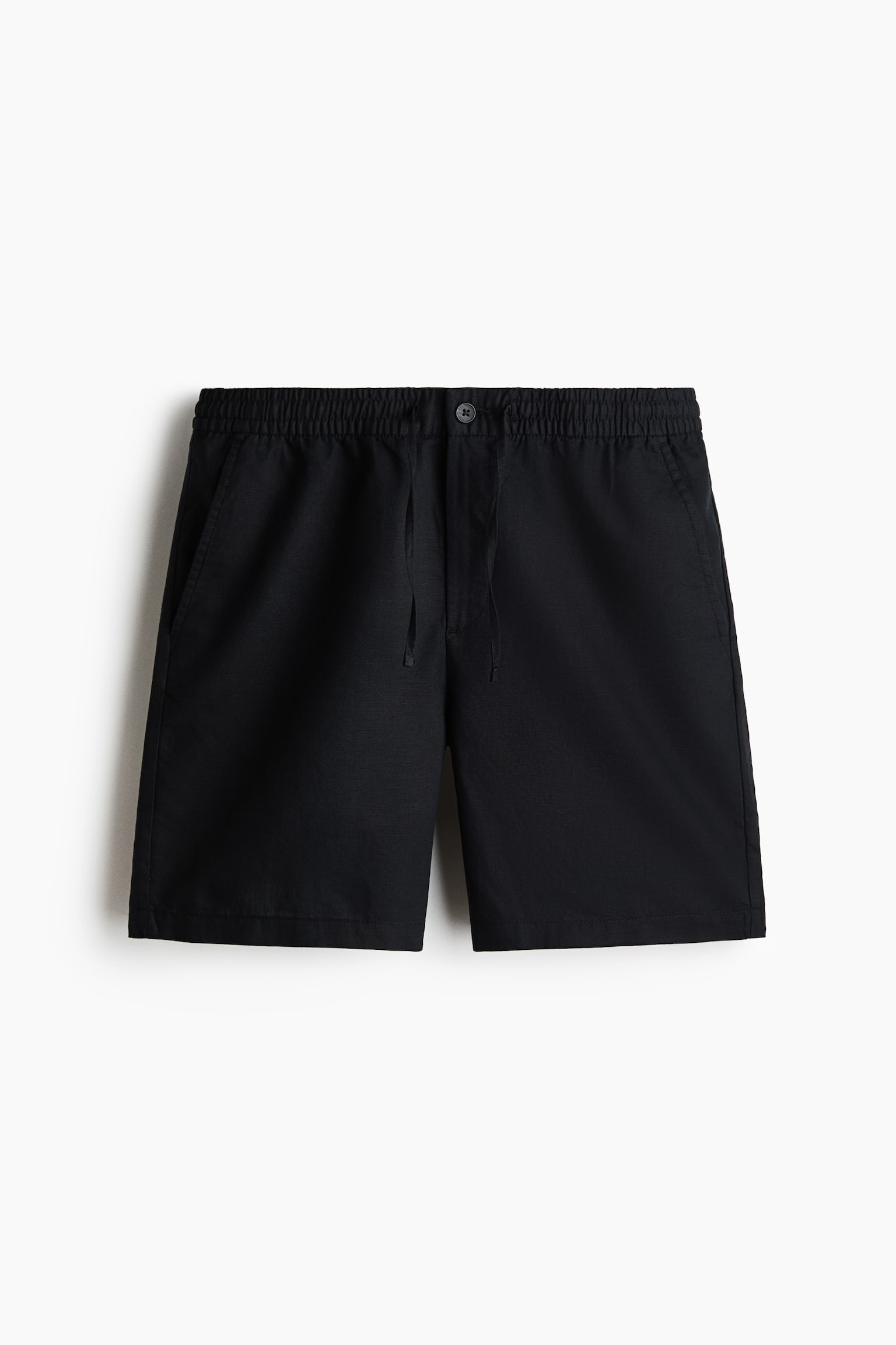 Los shorts negros están colocados de manera plana desde un ángulo frontal, mostrando un tejido texturizado de algodón y lino. Presentan una cintura elástica cubierta con cordón, un cierre de botón y bolsillos en las costuras laterales, indicando un ajuste regular. - 1