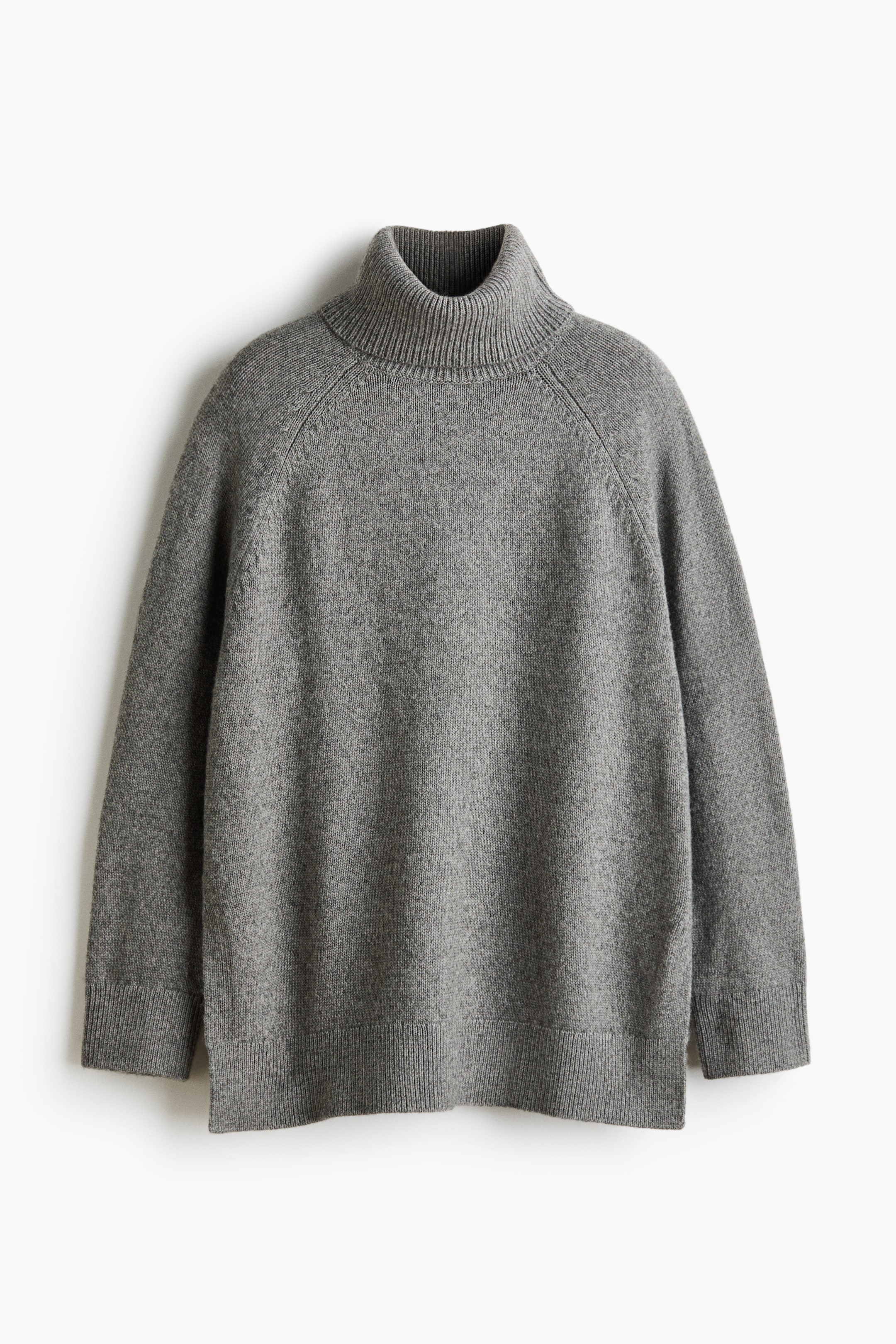 View larger image: A grey oversized jumper in a soft knit is shown from the front, featuring a ribbed polo neck and long raglan sleeves with ribbed cuffs. The relaxed silhouette falls to a ribbed hem with a small slit at each side.