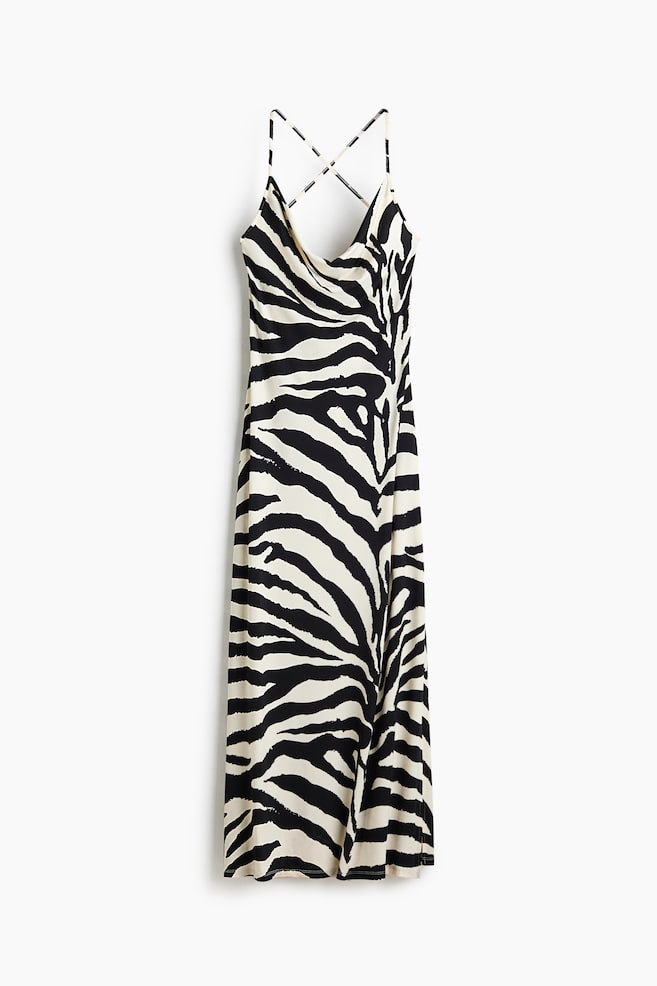 A zebra print slip dress features a cowl neck and thin straps that criss-cross at the back. It showcases black stripes on a cream backdrop and flows to a long length. - 1
