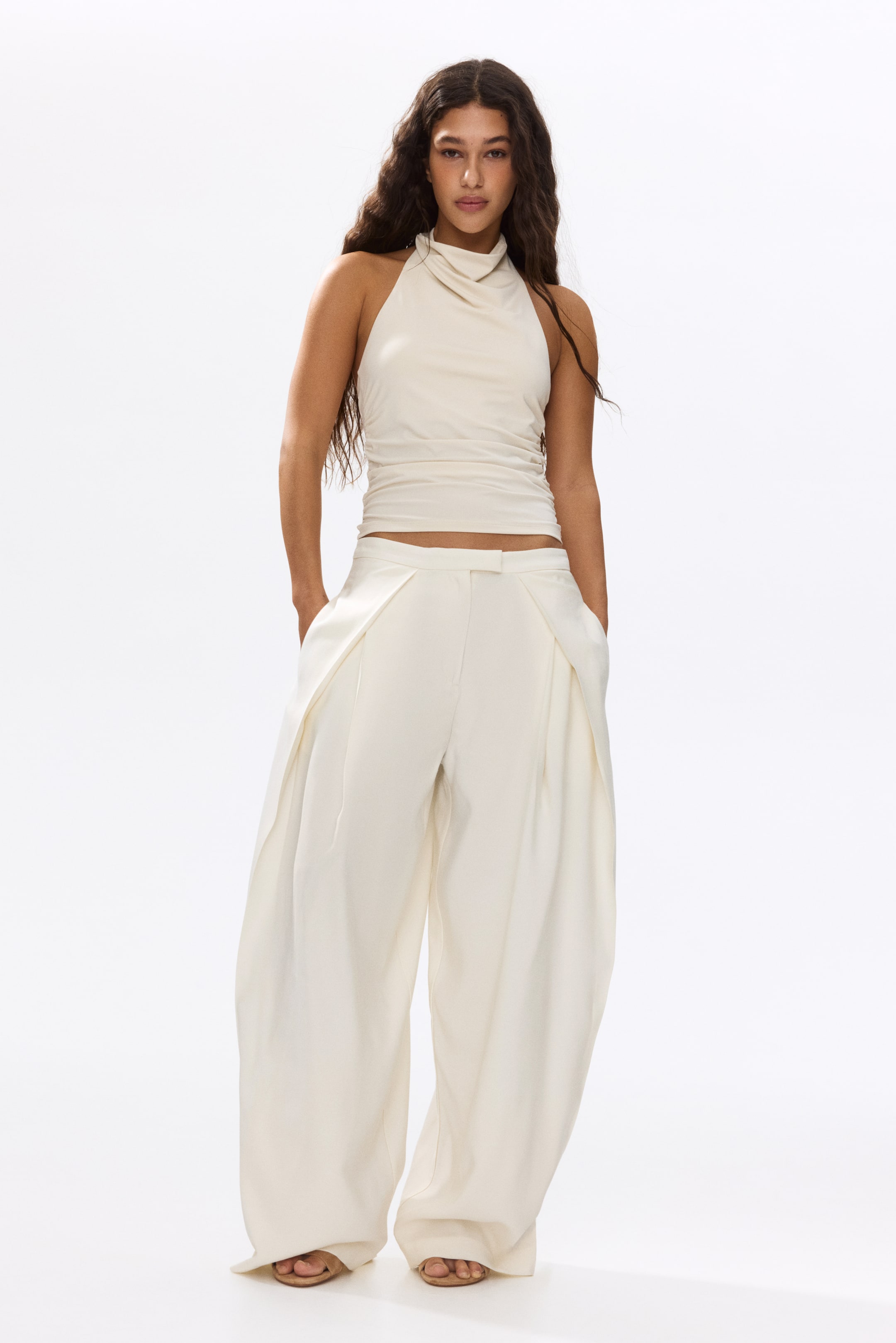 View larger image: Loose-fit twill trousers, featuring a high waist with an extended waistband and balloon legs with wrapover sides, are being worn by the model. The model is standing with her hands in the discreet side pockets.
