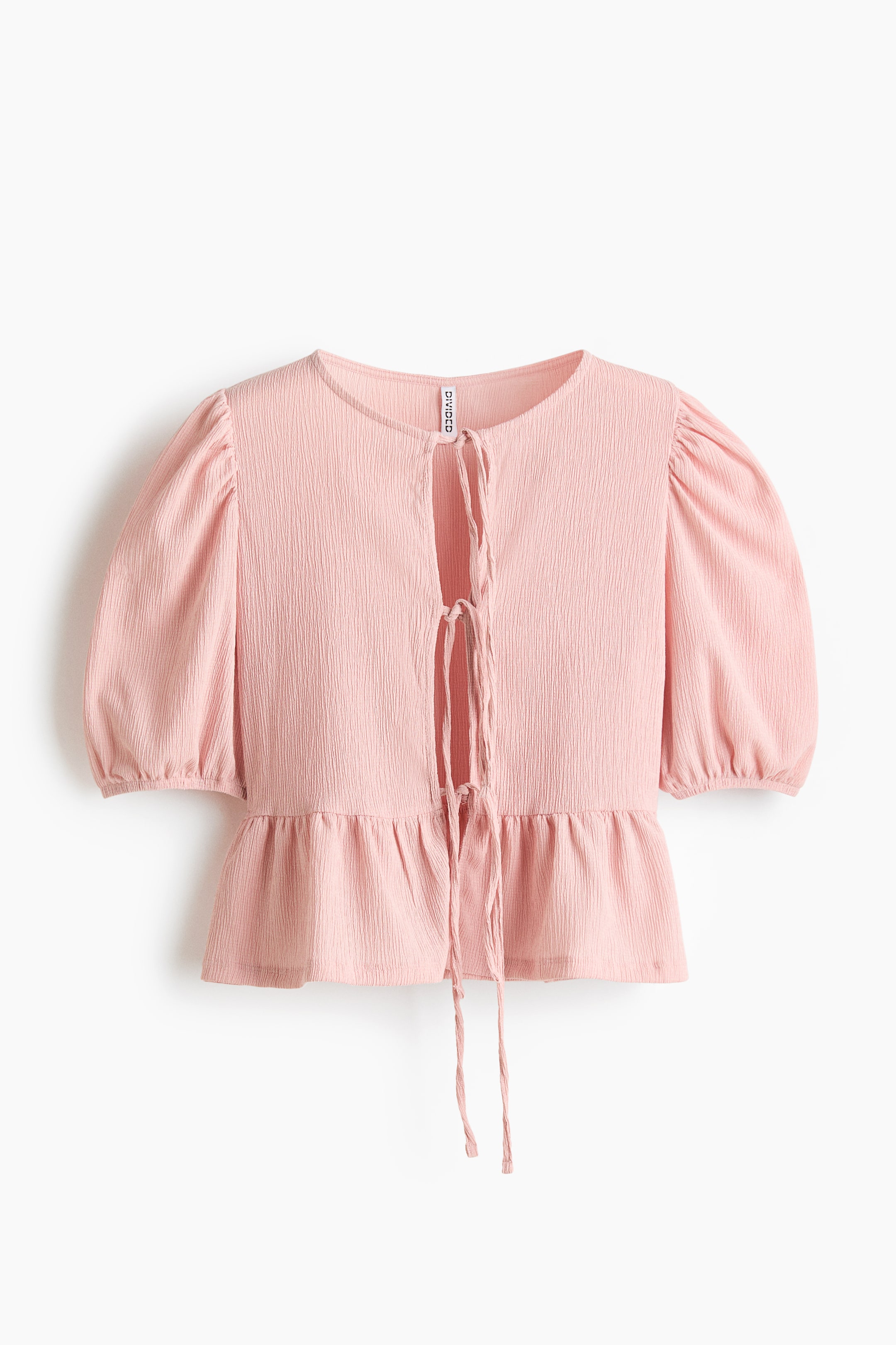 拡大画像を表示: ピンクのシワ加工トップスが正面に向けて配置されており、ラウンドネックとタイで留める前開き仕様が特徴です。パフのショートスリーブは袖口がゴム仕様で、裾はペプラムヘムになっています。