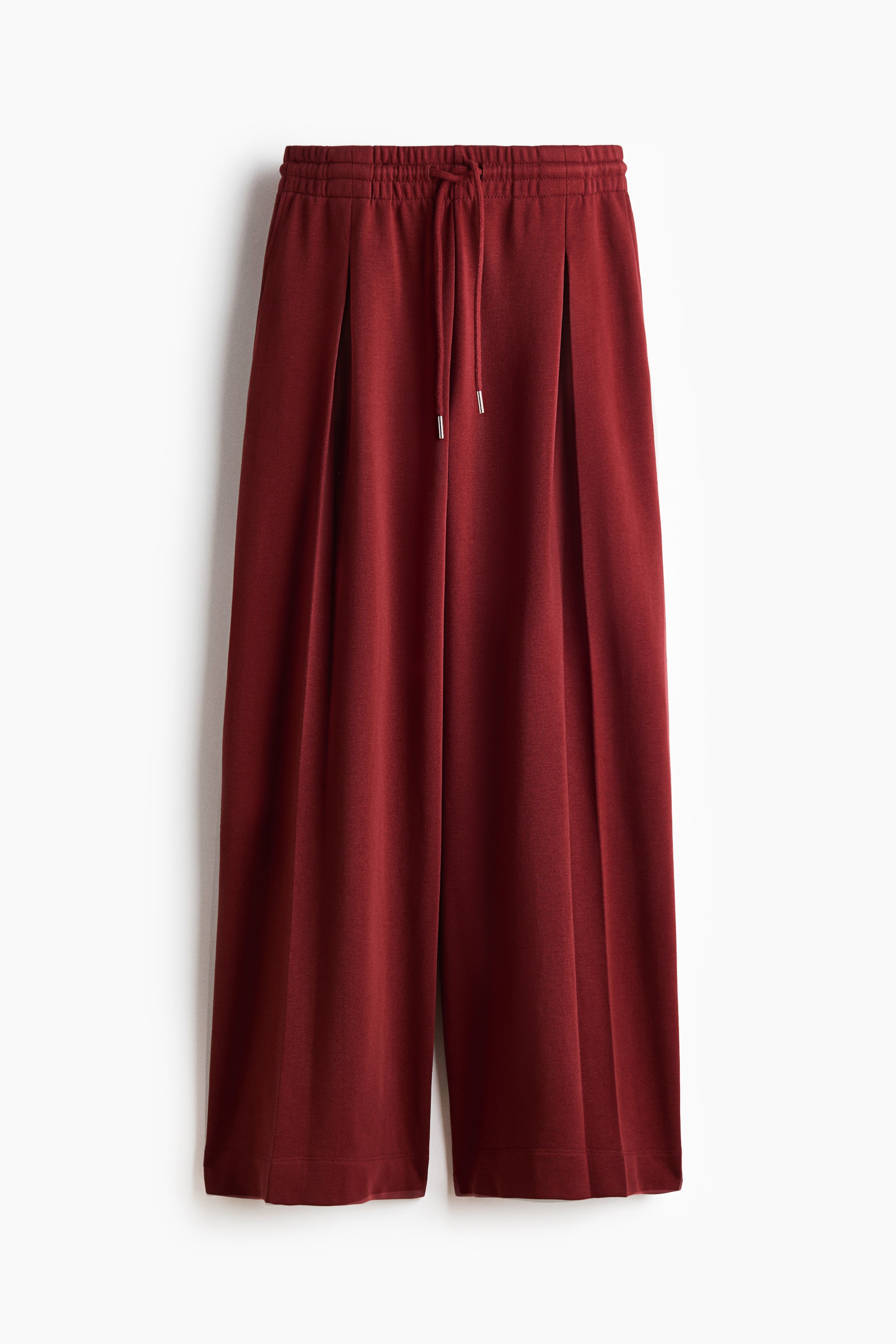 Grotere afbeelding bekijken: Dieprode, losvallende broek in lichte sweatshirtstof met een elastische tailleband en zilverkleurige trekkoorden, afgebeeld van de voorkant. Ontworpen met extra lange, wijde pijpen, elk voorzien van een omgekeerde stolpplooi aan de voorkant.
