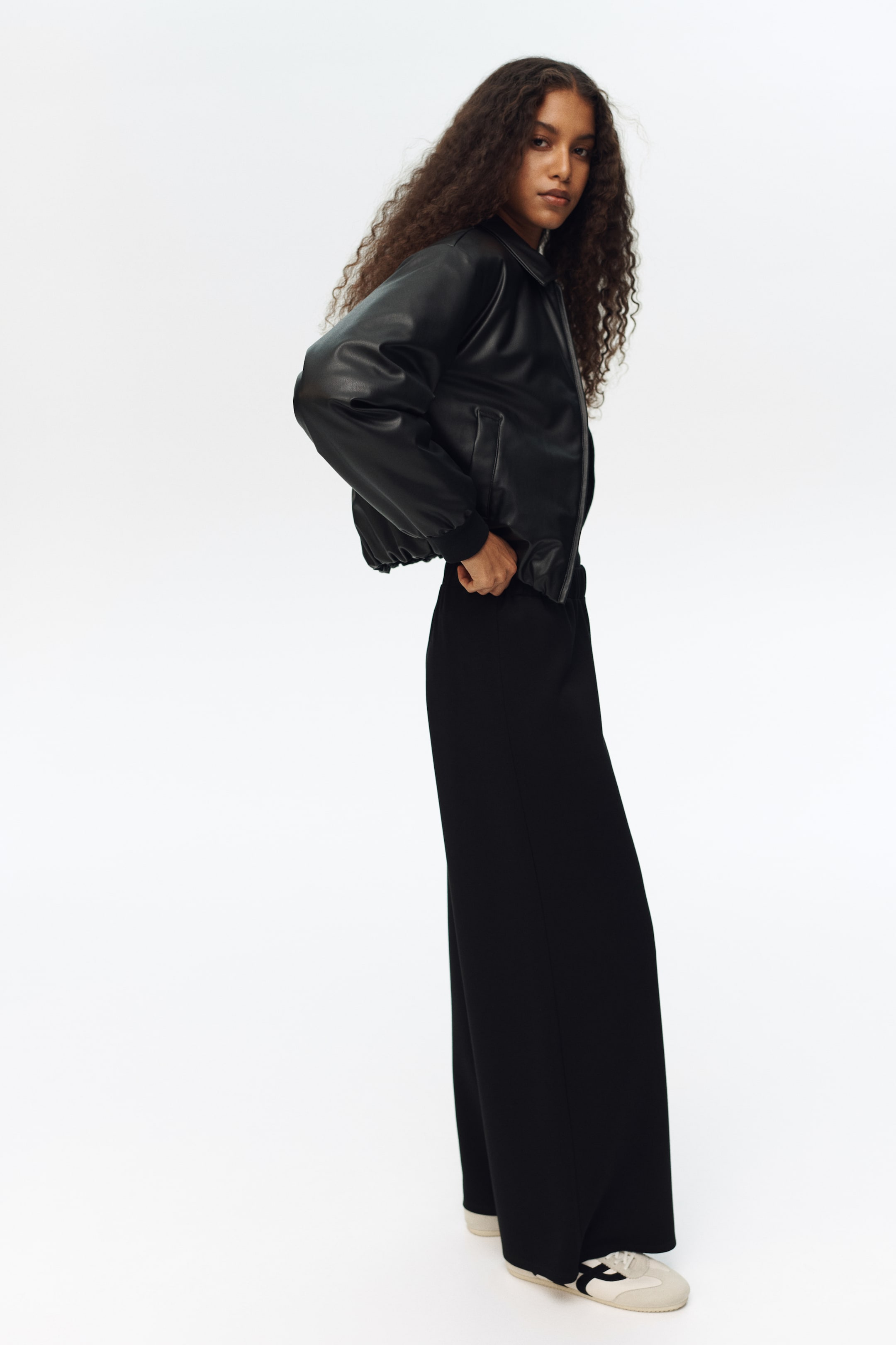 View larger image: "A black bomber jacket na gawa sa makinis, leather-like na materyal, may klasikong shirt collar, at ribbed cuffs at hem. Ipinapakita rin nito ang dalawang front welt pockets at isang relaxed, bahagyang cropped fit, na ipinapakita mula sa side-front na anggulo."