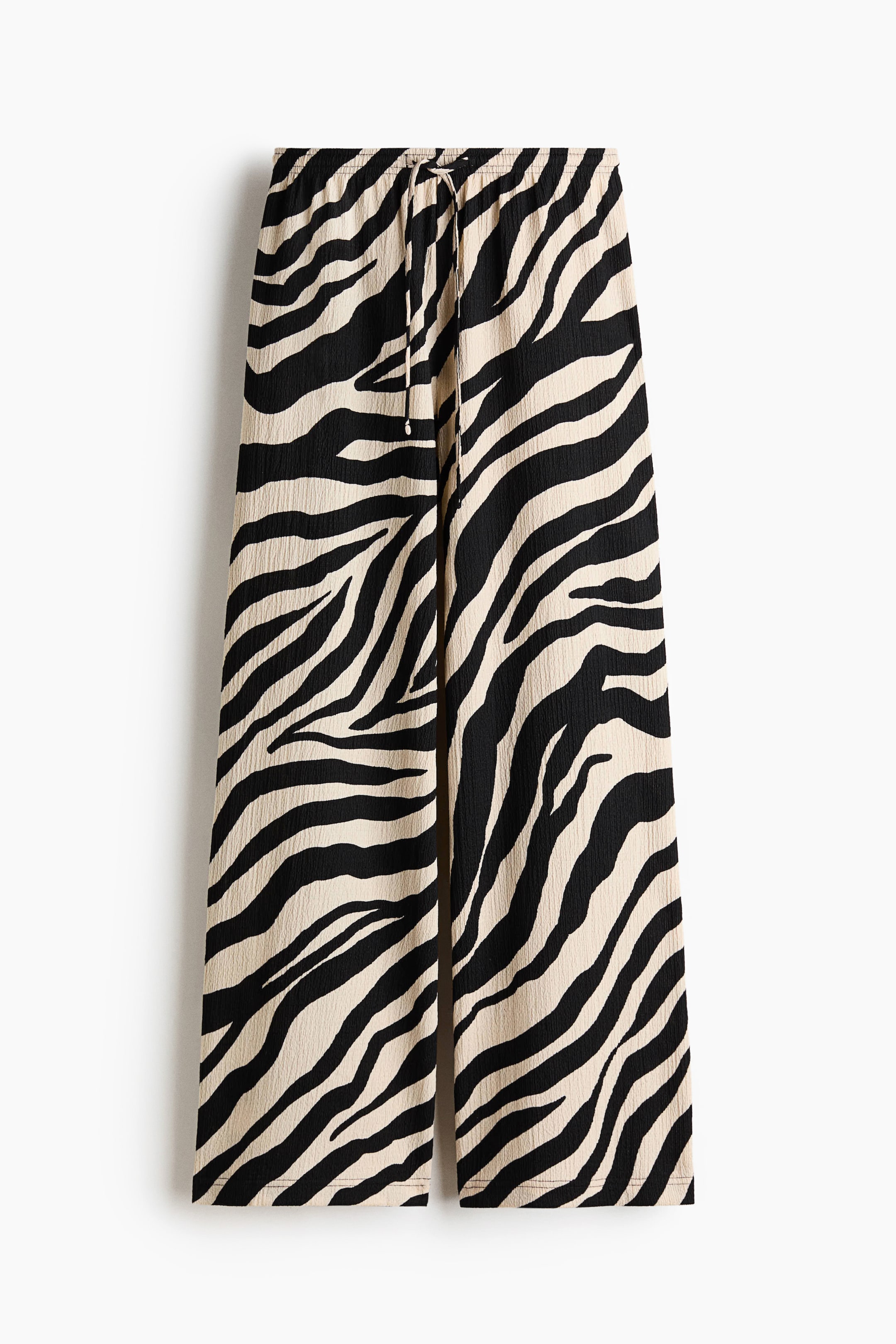 View larger image: Loose-fit jersey trousers showcase a black and beige zebra print, viewed from the front. They feature a high, elasticated drawstring waist, tied at the center, and wide legs.