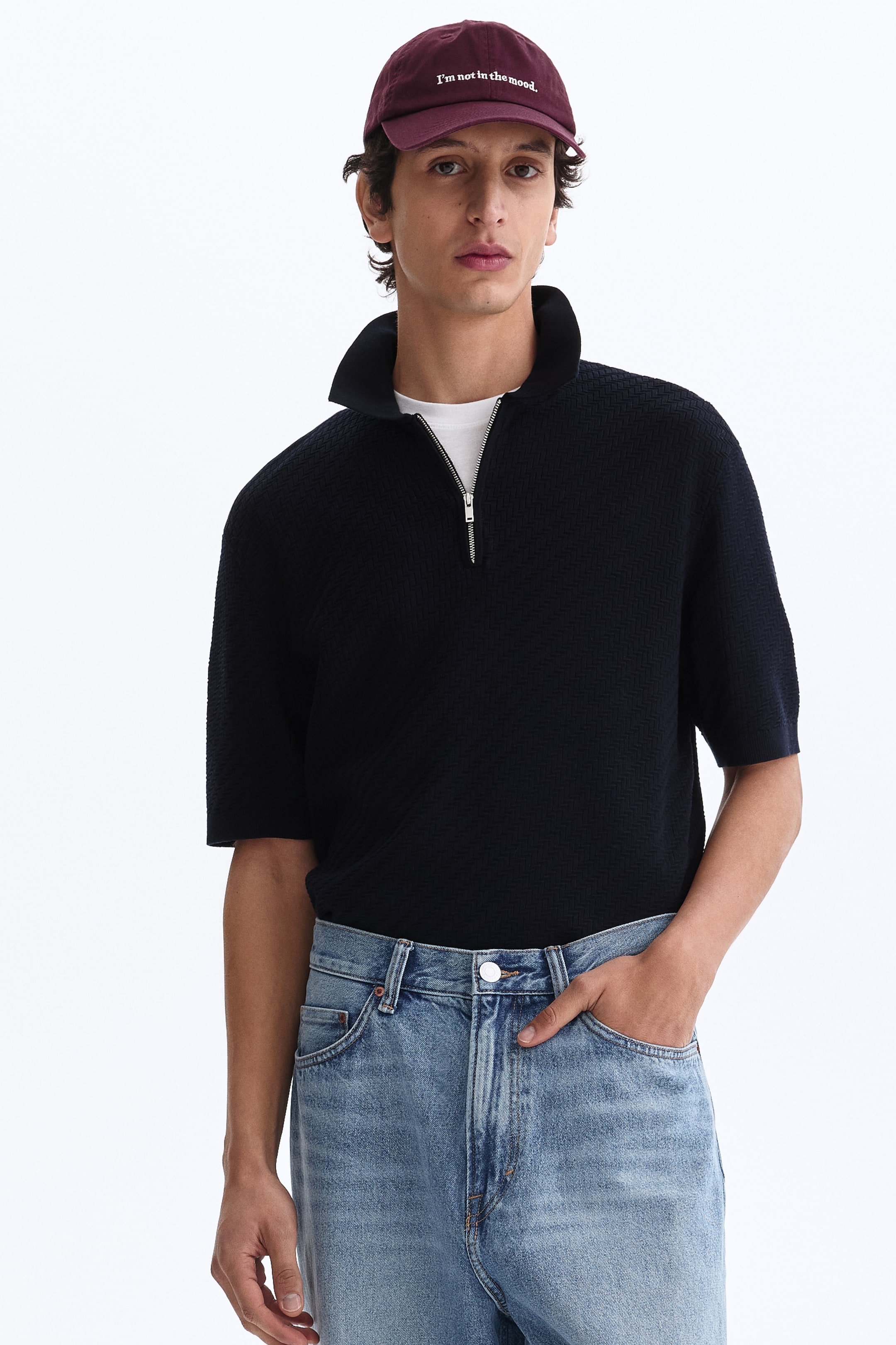View larger image: A dark short-sleeved top featuring textured knit fabric, a stand-up collar, and a silver half-zip closure, worn over a white T-shirt.