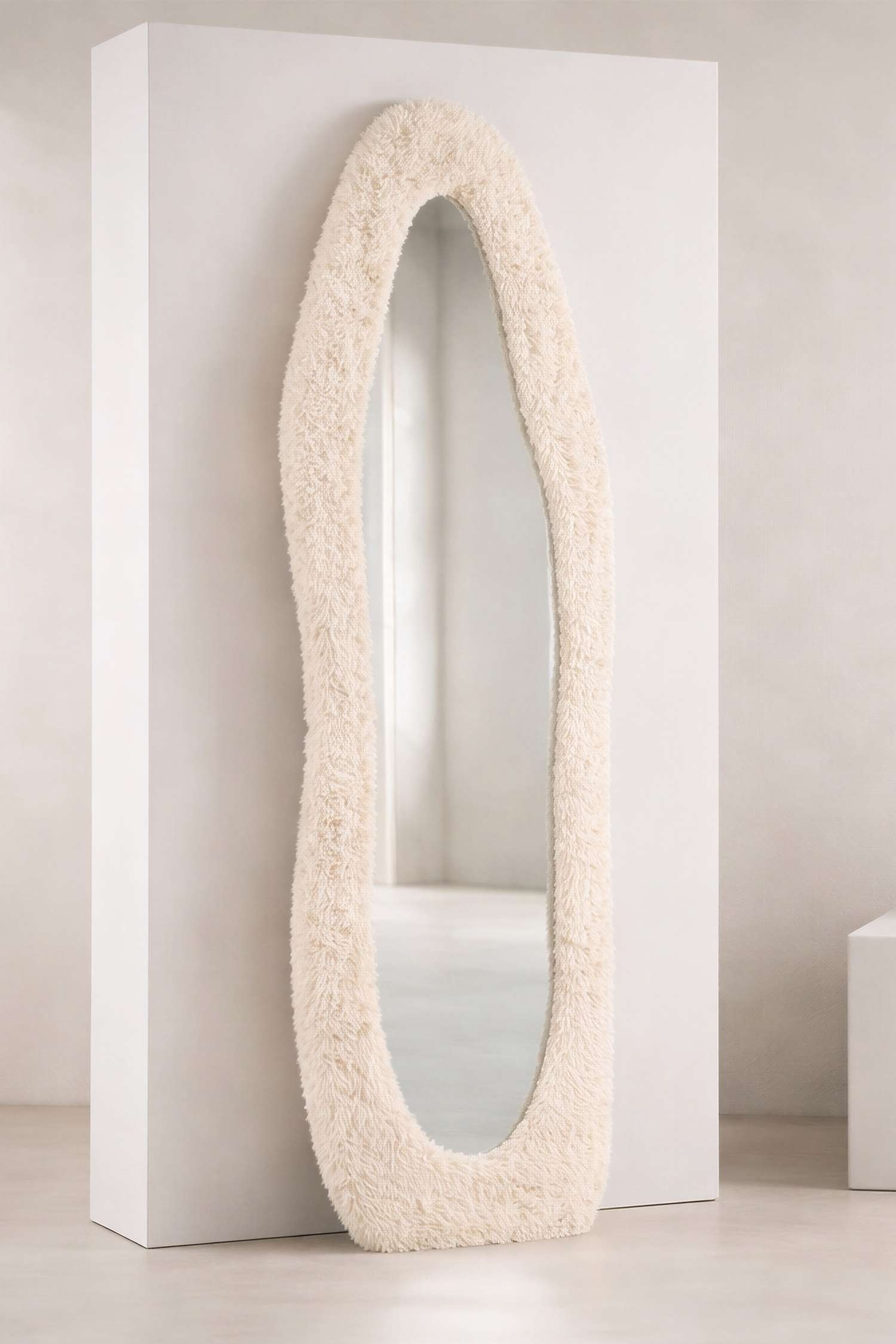 Un espejo muestra una forma irregular y orgánica. Presenta un marco grueso, de color beige claro, con textura que rodea una superficie reflectante.