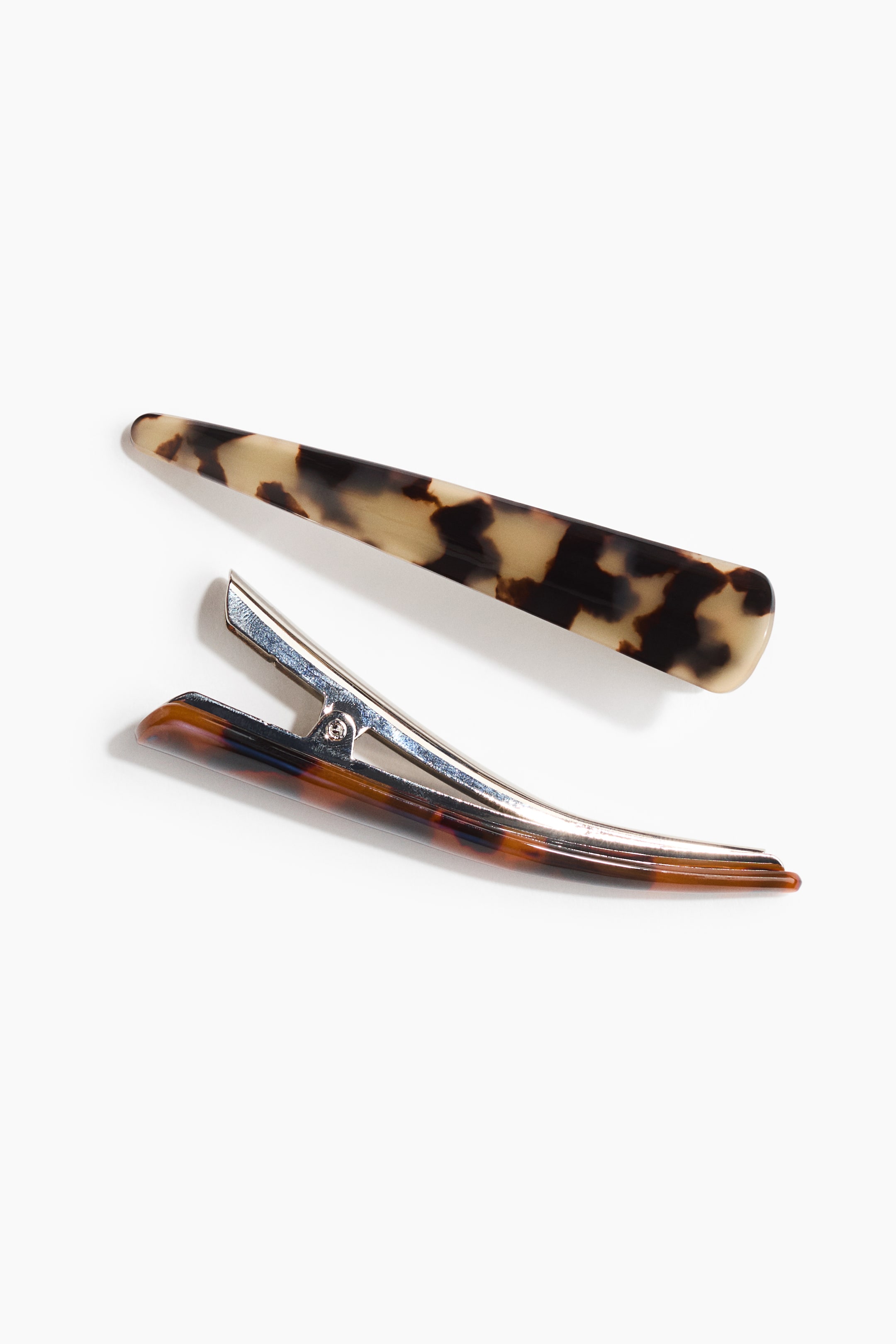 View larger image: Two hair clips with a tortoiseshell pattern are arranged diagonally, featuring a flat, tapered barrette on top and a duckbill-style clip beneath it. The duckbill clip boasts a silver-toned metal mechanism and a tortoiseshell pattern on its exterior.