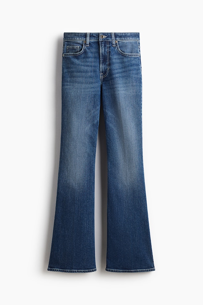 VORDERSEITE: Ein Paar blaue Denim-Jeans präsentiert einen hohen Bund mit einem Reißverschluss und Knopfverschluss. Es verfügt über Vordertaschen und eine Münztasche, eine schmale Passform durch Taille und Oberschenkel und einen ausgestellten Schnitt vom Knie bis zum Saum, mit einer langen Länge, die dazu gedacht ist, am Fuß zu stapeln. - 1