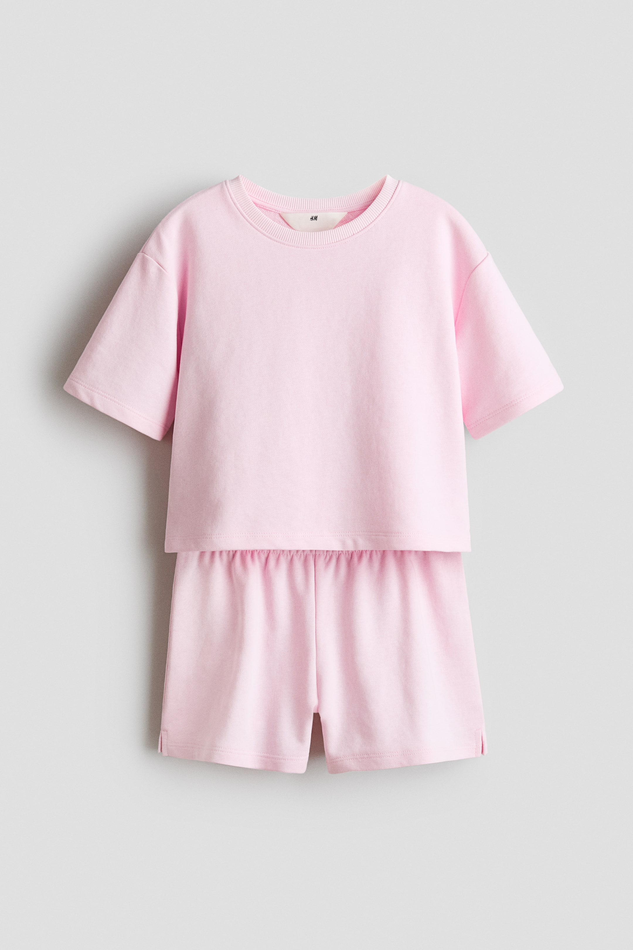 查看大圖: 粉紅色舒適套裝展示其正面,T 恤具有圓形羅紋邊領口、落肩設計,以及直剪下擺,兩側開有小裂口。配套短褲腰部為隱藏式鬆緊設計。