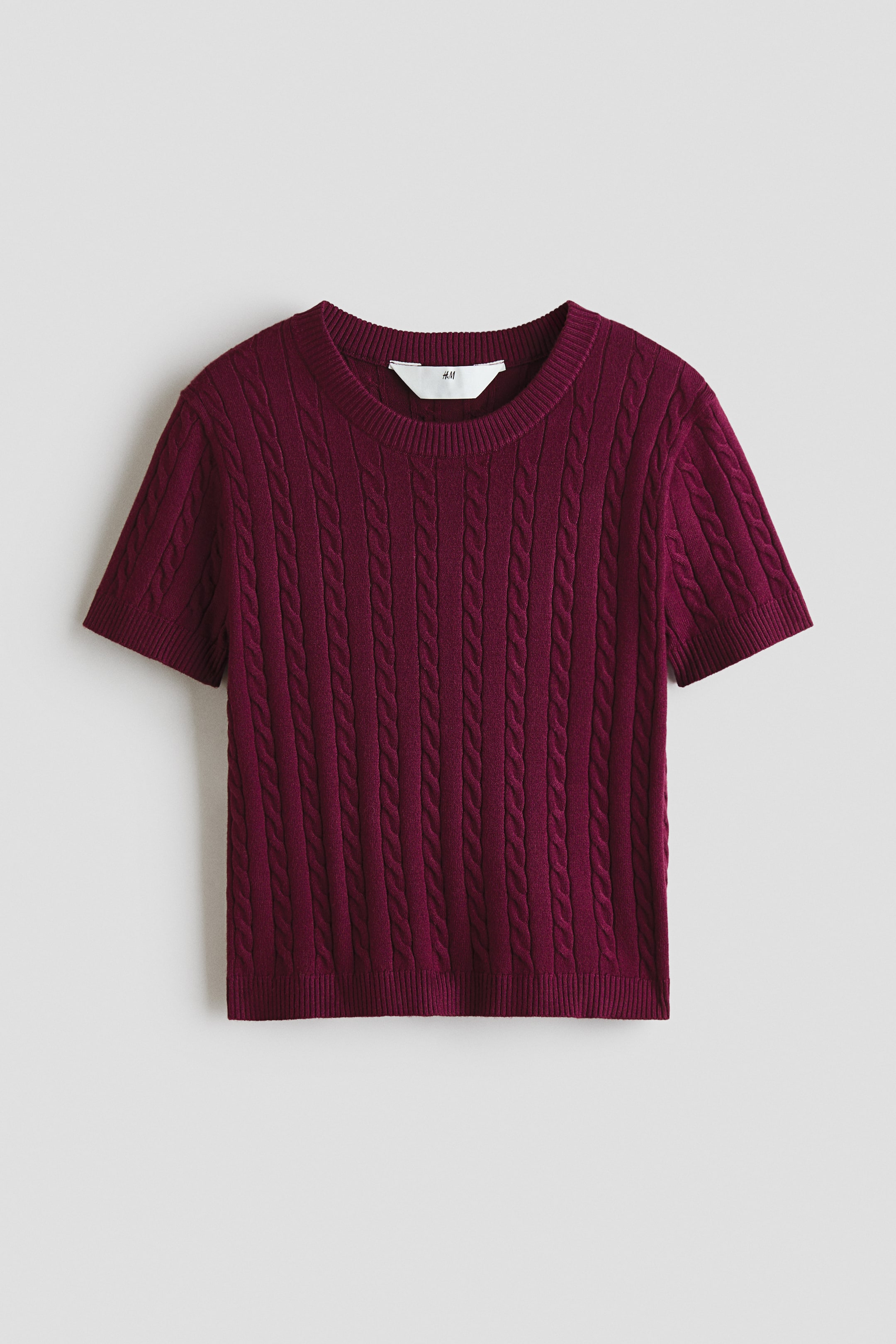 View larger image: A deep red short top is lying flat, showcasing its cable knit texture, a round rib-trimmed neckline, short sleeves with ribbed cuffs, and a ribbed hem.