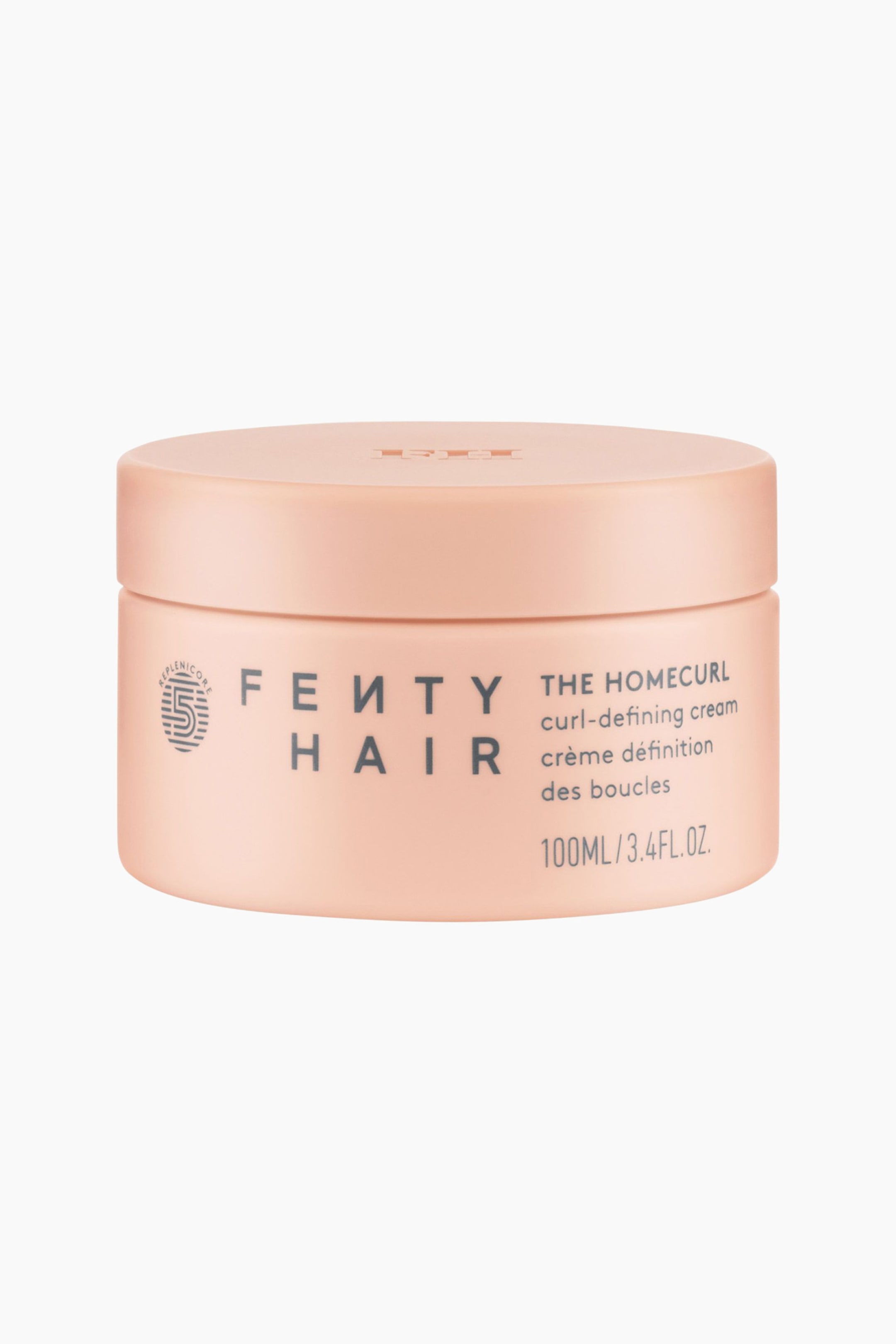 Visa större bild: Homecurl Curl-defining Cream Mini står upprätt och vänd framåt och har en cylindrisk, matt persikofärgad burk med ett matchande skruvlock. På framsidan av behållaren visas logotypen "FENTY HAIR", produktnamnet och volyminformationen tryckt i mörkgrå text.