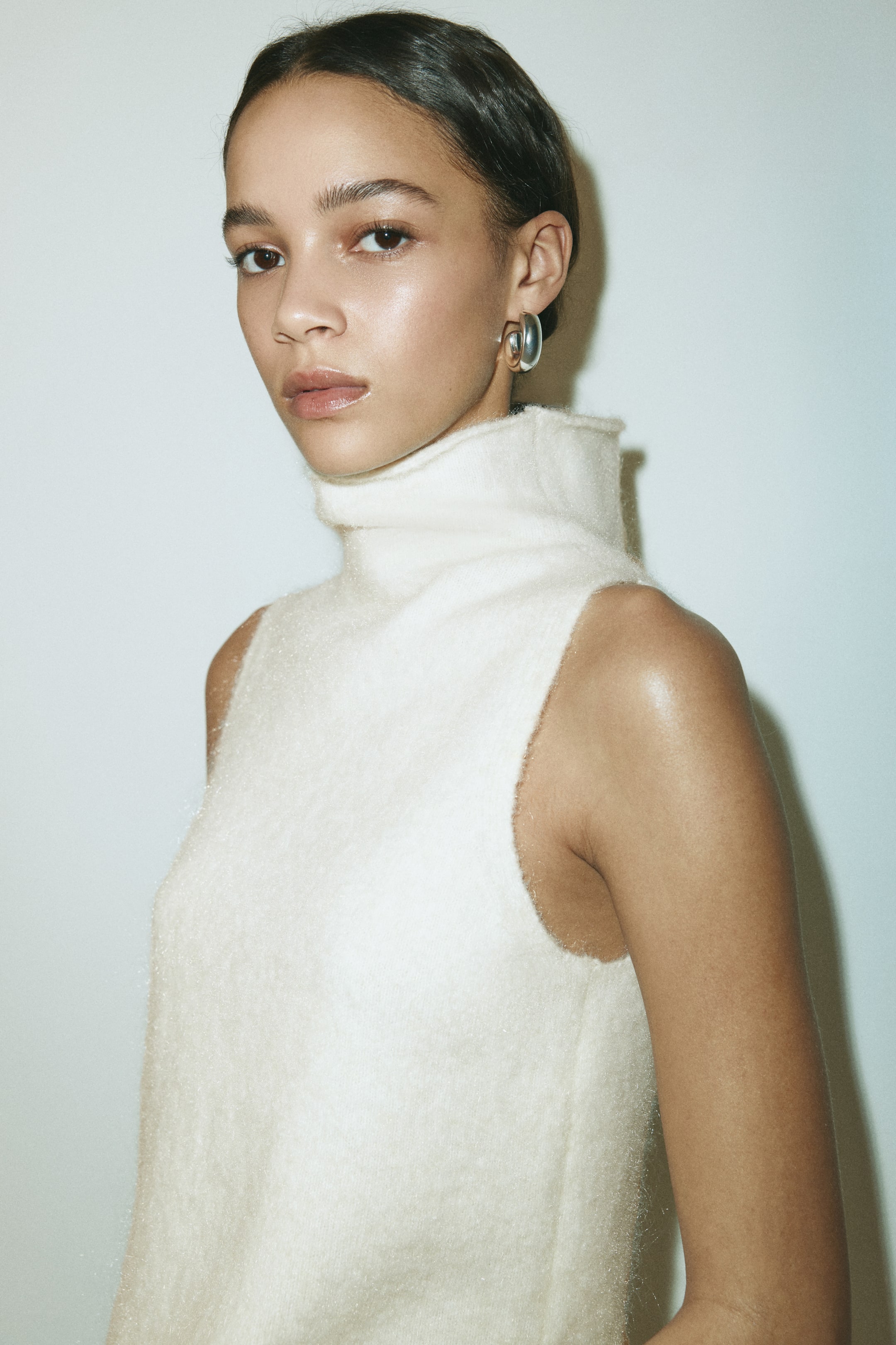 View larger image: An off-white sleeveless top is shown from a slight front-right angle, featuring a high turtleneck. It showcases a fuzzy, brushed texture and clean-cut armholes.