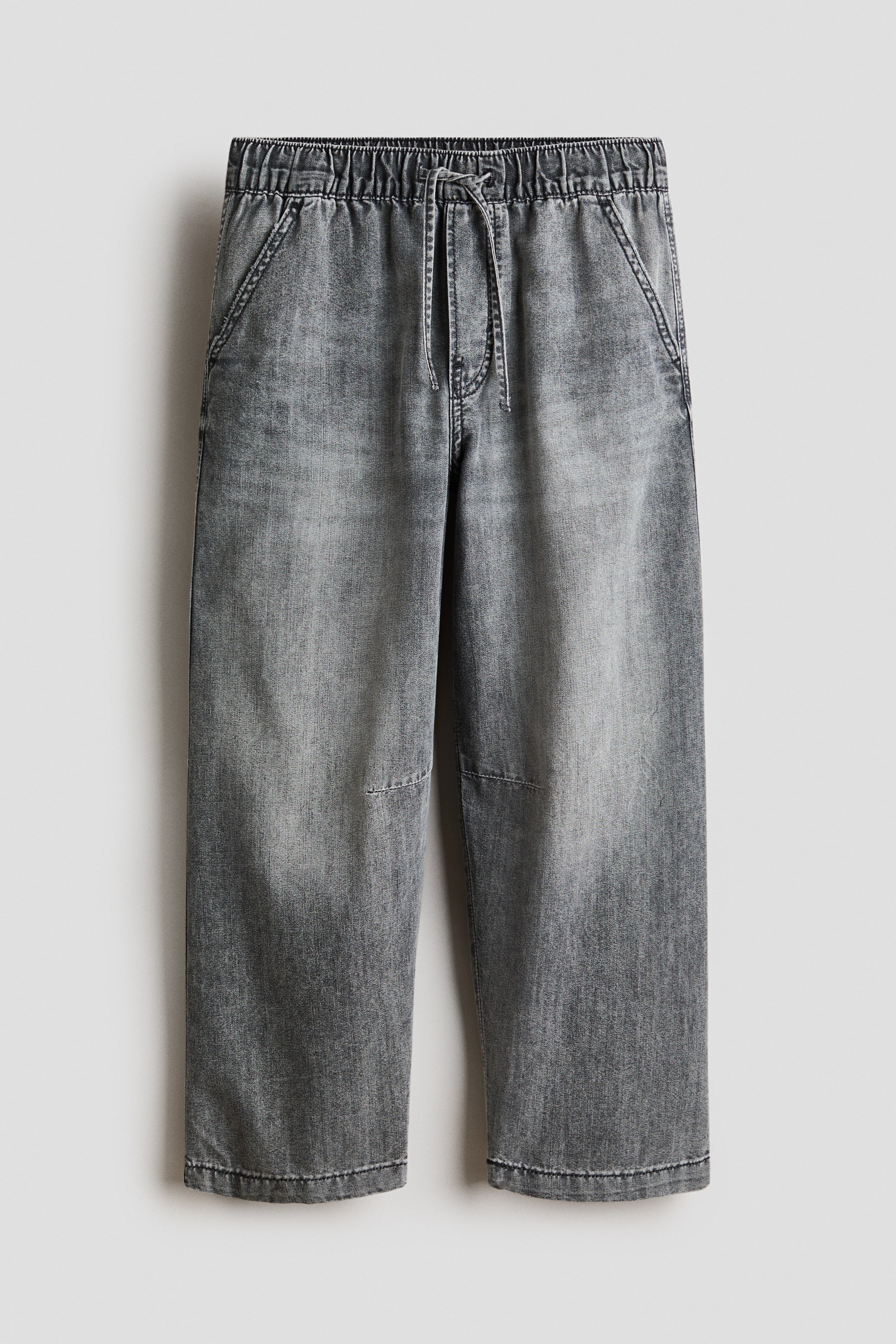 Ver imagen más grande: Los pantalones grises cuentan con una cintura elástica con un cordón visible. Presentan bolsillos frontales inclinados, y el material de mezclilla muestra un lavado desgastado con detalles de costura sutiles en las piernas inferiores.