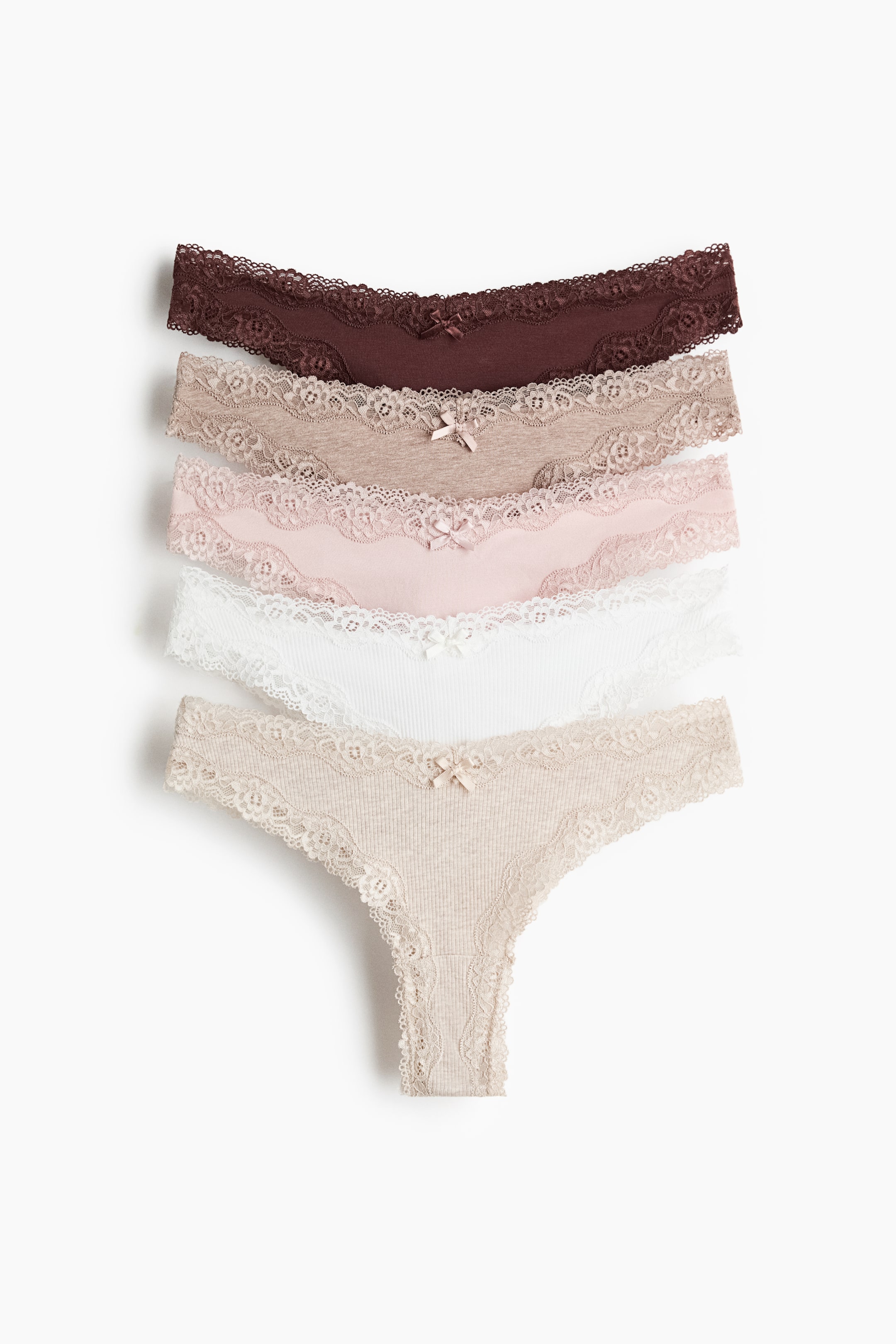 Büyük resmi görüntüle: Beş pamuklu jarse külot, üst üste binen, öne bakan bir yığın halinde sunuluyor, her biri V şeklinde bir bel hattı, küçük bir orta fiyonk ve kenarlarında dantel süslemelerle dikkat çekiyor. Koyu kahverengi, açık kahverengi, pembe, beyaz ve bej tonlarında görünüyorlar, alttaki iki tanesi ise kabartmalı bir doku sergiliyor.