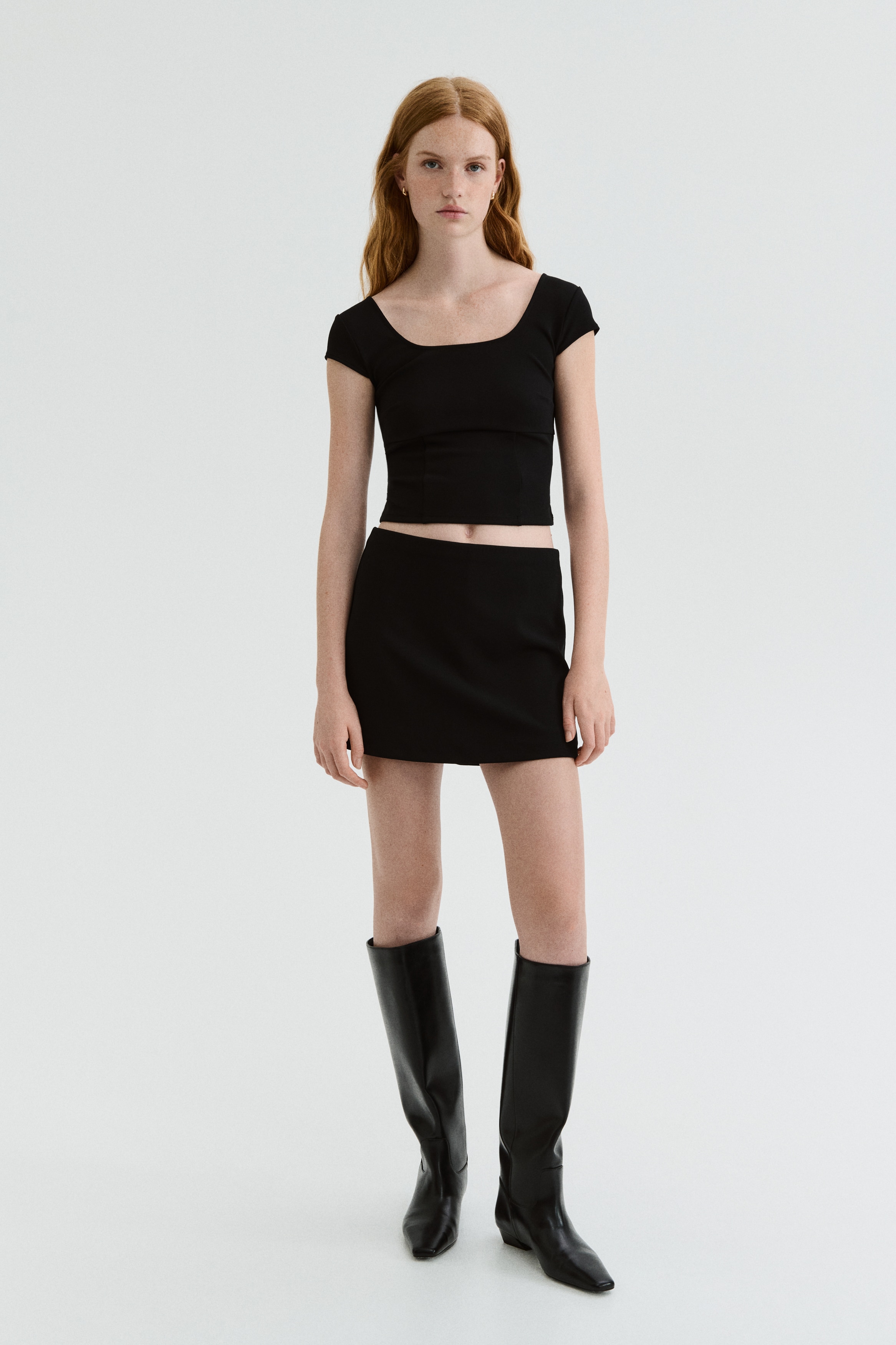 A black, short, fitted skort is displaying its front view, featuring an elasticated waist and jersey fabric.