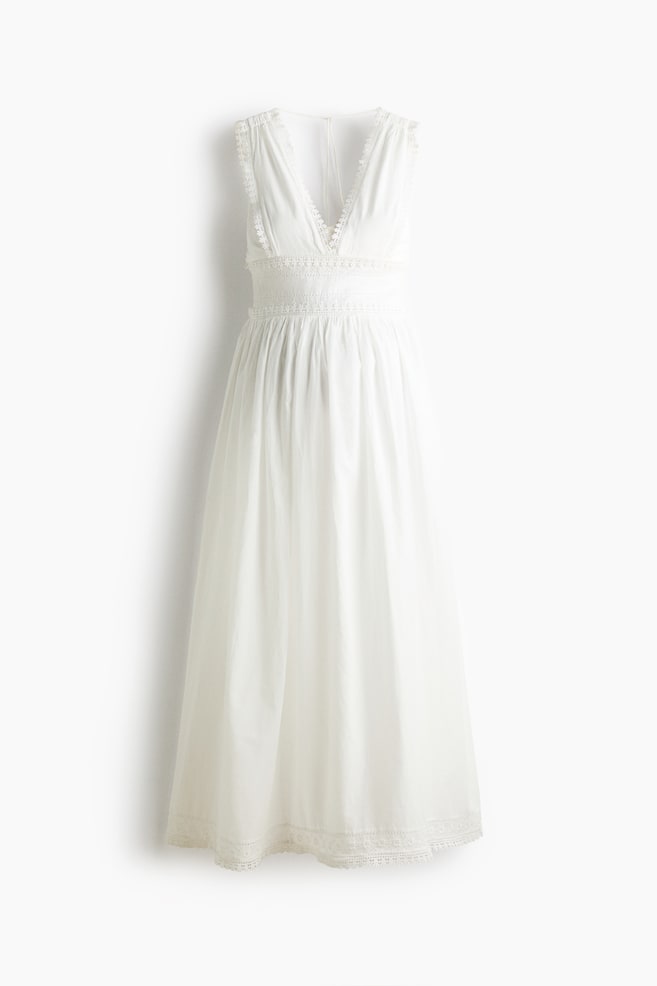 Ein langes, Ã¤rmelloses weiÃes Baumwoll-Stillkleid wird von vorne gezeigt und verfÃ¼gt Ã¼ber einen tiefen V-Ausschnitt mit zarter Spitzenborte am Oberteil und an den TrÃ¤gern. Das Kleid ist mit einer gerafften Taille, einem bestickten Unterbrustband und einem sanft ausgestellten Maxirock gestaltet, der mit einem spitzenverzierten Saum abschlieÃt. - 1