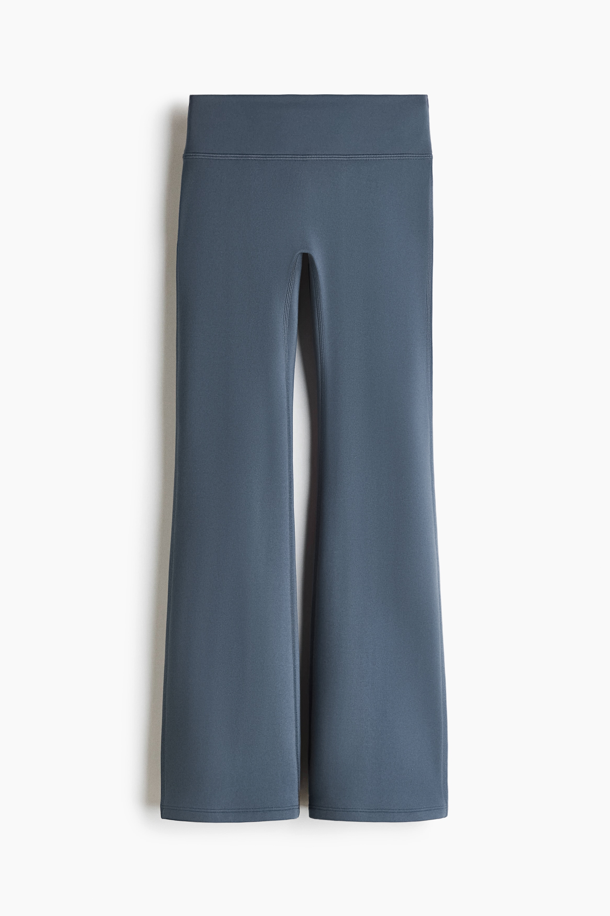Un jersey polar azul marino con cuello alto y mangas largas se lleva con unos leggings acampanados de color verde azulado oscuro, ajustados en el muslo y que se ensanchan hacia el bajo.