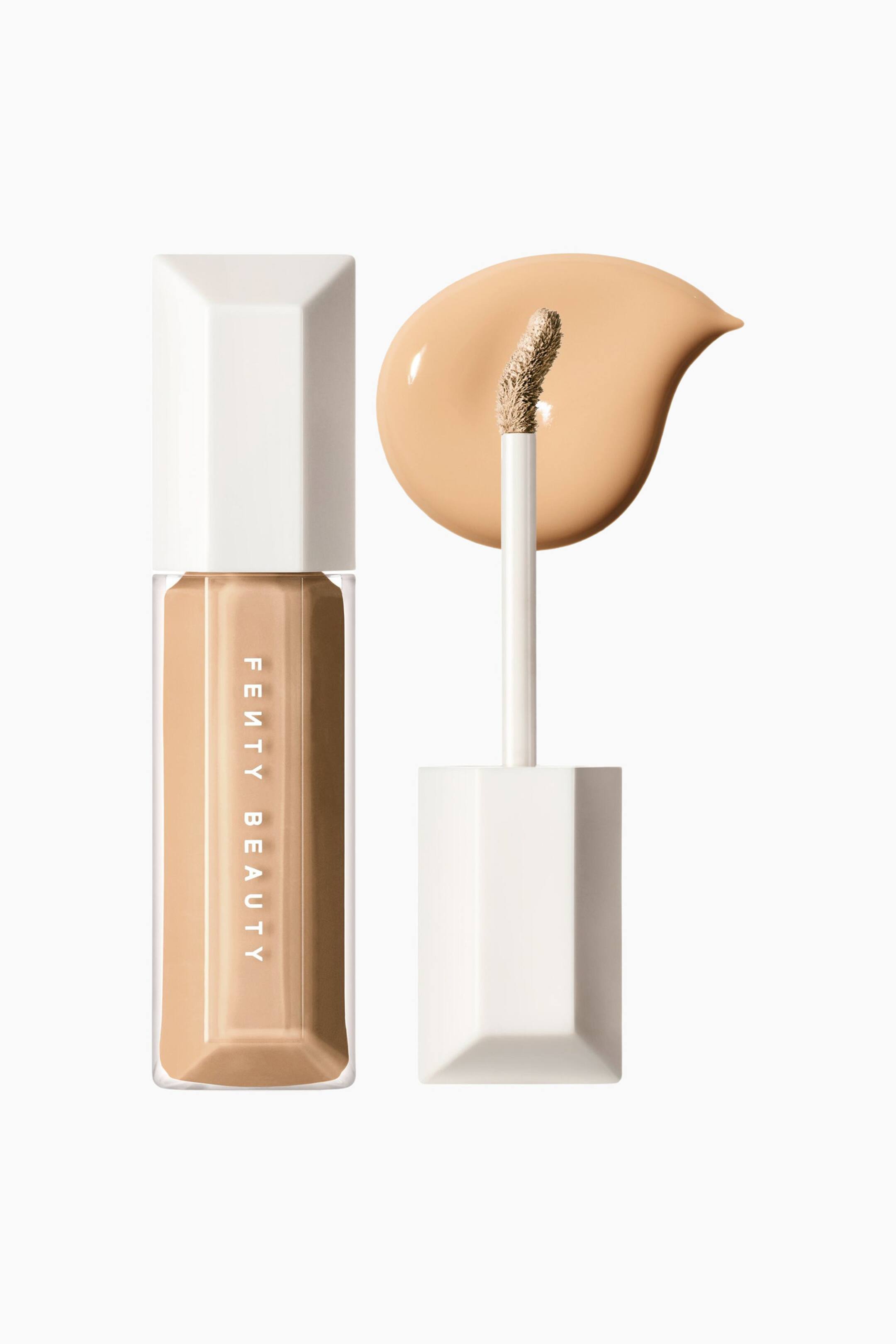 Visa större bild: We're Even Hydrating Longwear Concealer står upprätt i en genomskinlig, facetterad flaska med vit kork och visar upp sin ljus-mediumbeige nyans. En separat applikatorstav står lodrätt bredvid den och visar en böjd, produktbelagd doe-foot-spets framför en slät, droppformad flytande färgfläck.