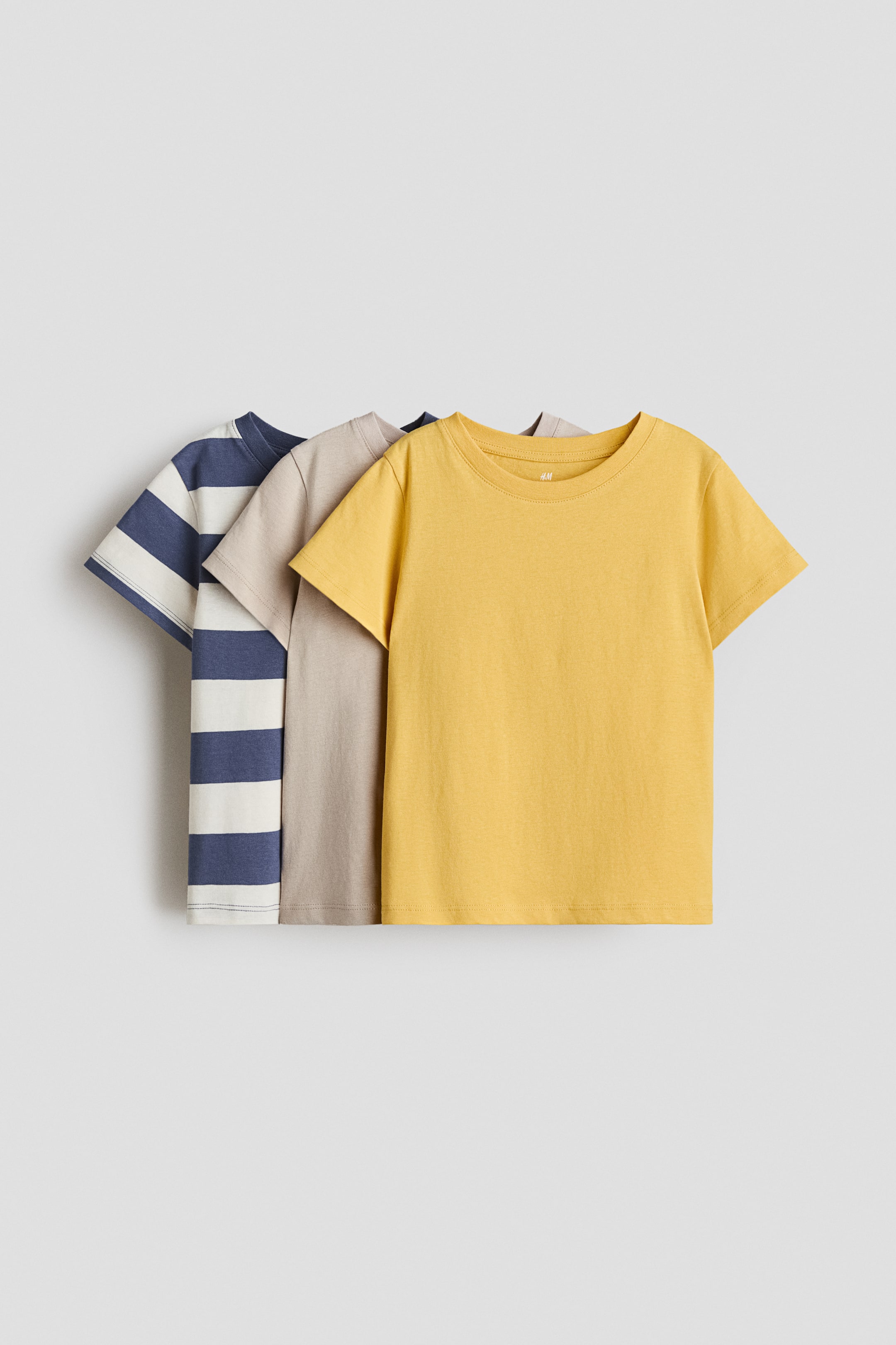 View larger image: A set of three t-shirts is displaying, facing FRONT, with the foremost t-shirt featuring a solid yellow color, the middle t-shirt showcasing a solid beige, and the rearmost t-shirt presenting navy blue and off-white horizontal stripes. All t-shirts are featuring crew necks and short sleeves.