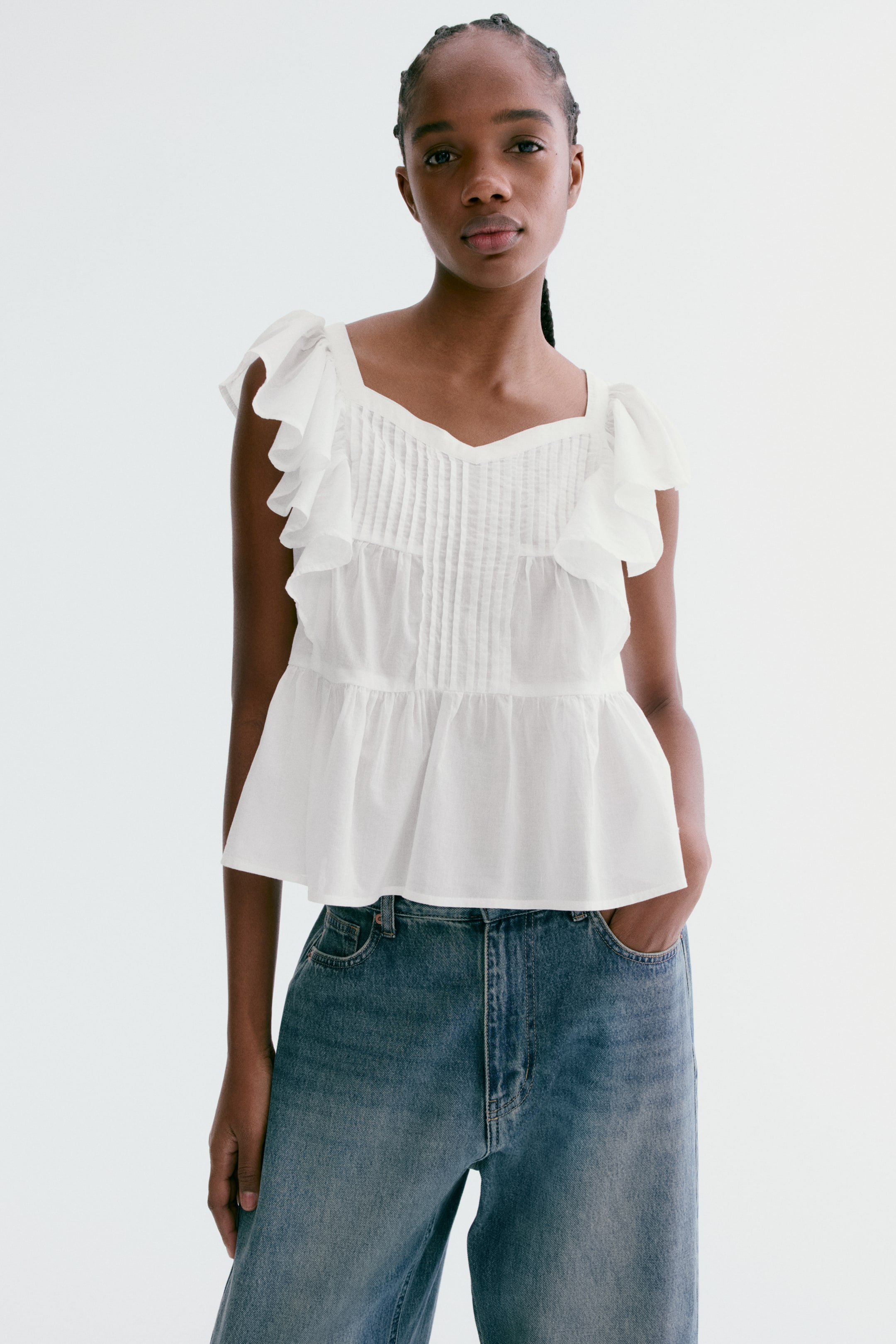 View larger image: This white top showcases a square neckline, ruffled cap sleeves, and V-shaped pintuck detailing on the upper bodice, complemented by a gathered peplum hem that elegantly flows over blue jeans.