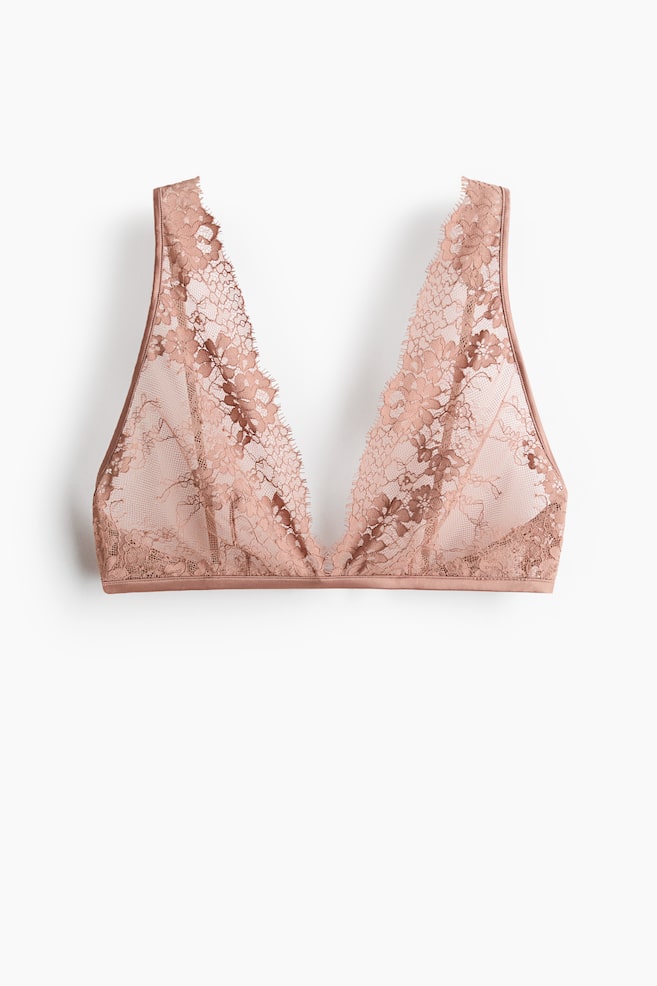 A blush pink lace bralette is lying flat, showcasing a deep V-neckline with scalloped lace edges and a sheer floral pattern, featuring a thin band along its bottom. - 1