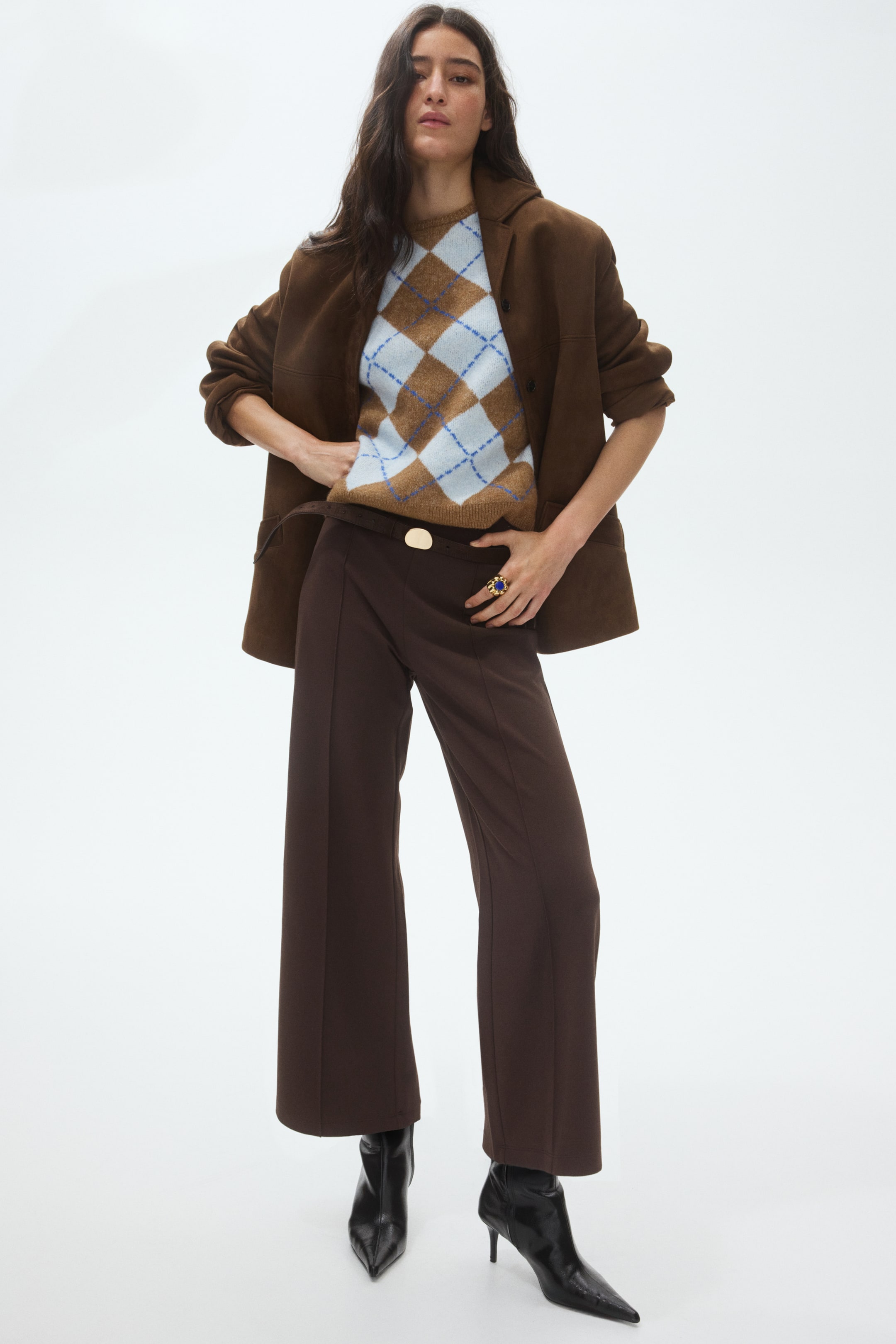 View larger image: The product showcases a complete ensemble, angled slightly to the right, featuring a brown oversized jacket with notch lapels layered over a brown argyle jumper with light blue and dark blue diamond patterns. The jumper is partially tucked into dark brown wide-leg trousers, which are secured with a gold-coloured buckle at the waist, and black pointed-toe ankle boots with stiletto heels complete the look.