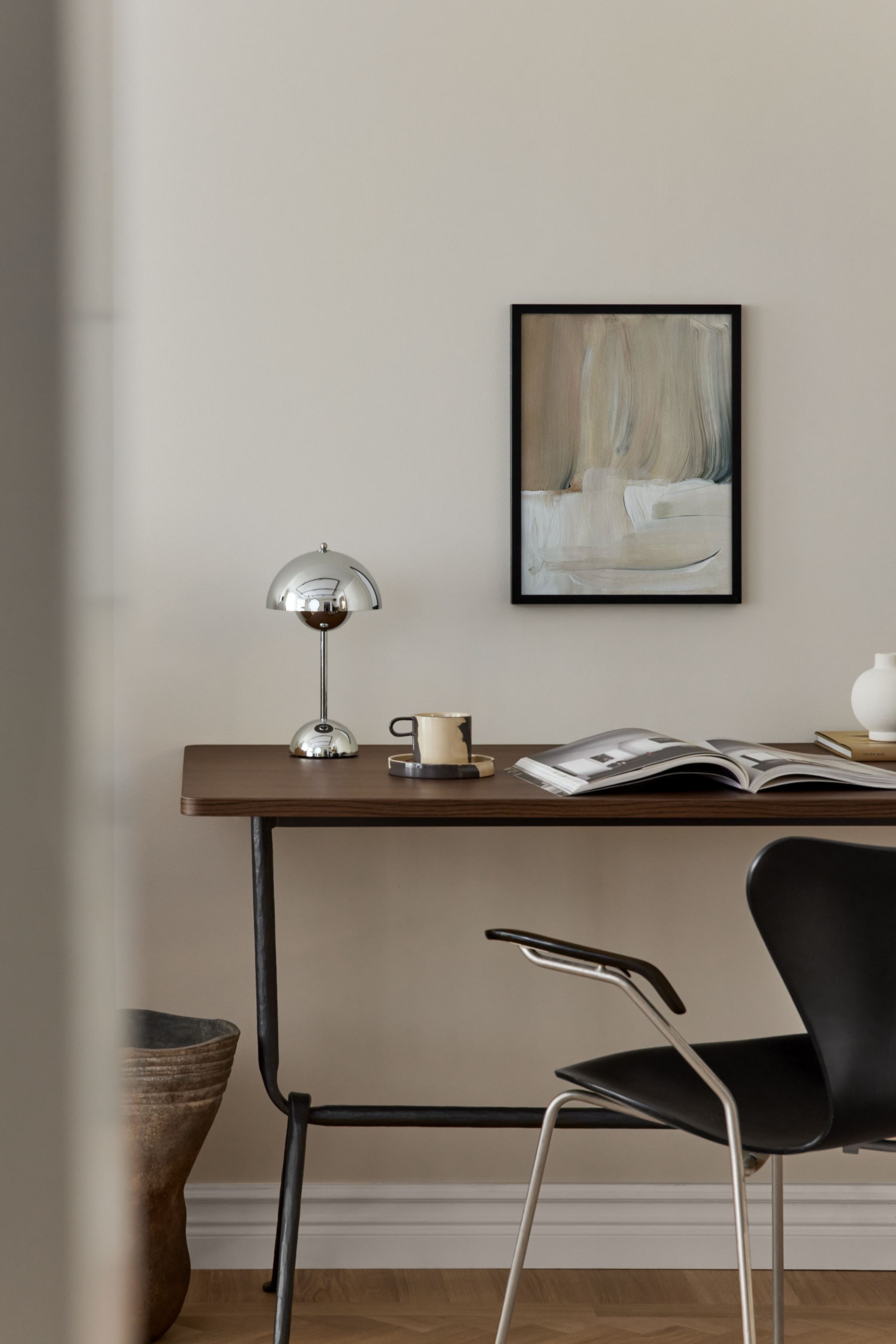 Grotere afbeelding bekijken: Een chromen tafellamp met een gepolijste, halfronde kap, een slanke stang en een ronde voet. Het staat op een donkerbruin houten bureau.