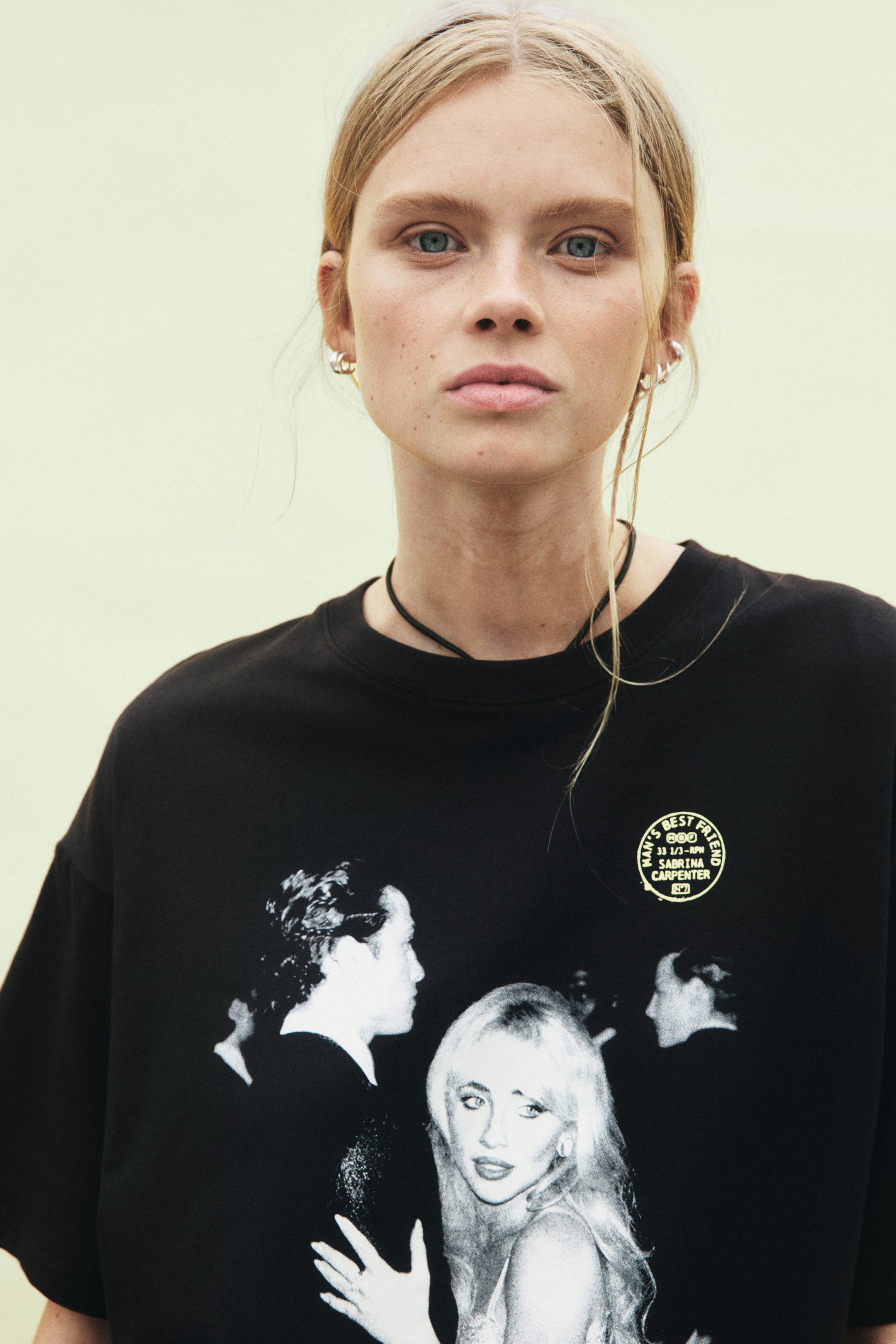 Größeres Bild ansehen: Das Model trägt ein oversized T-Shirt aus weichem schwarzem Baumwolljersey. Das Shirt ist mit einem gerippten Rundhalsausschnitt und überschnittenen Schultern gestaltet. Auf der Vorderseite zeigt es einen großen schwarz-weißen Fotoprint mit mehreren Figuren, zudem ist auf der oberen Brust ein kleiner runder gelber Grafikprint zu sehen.
