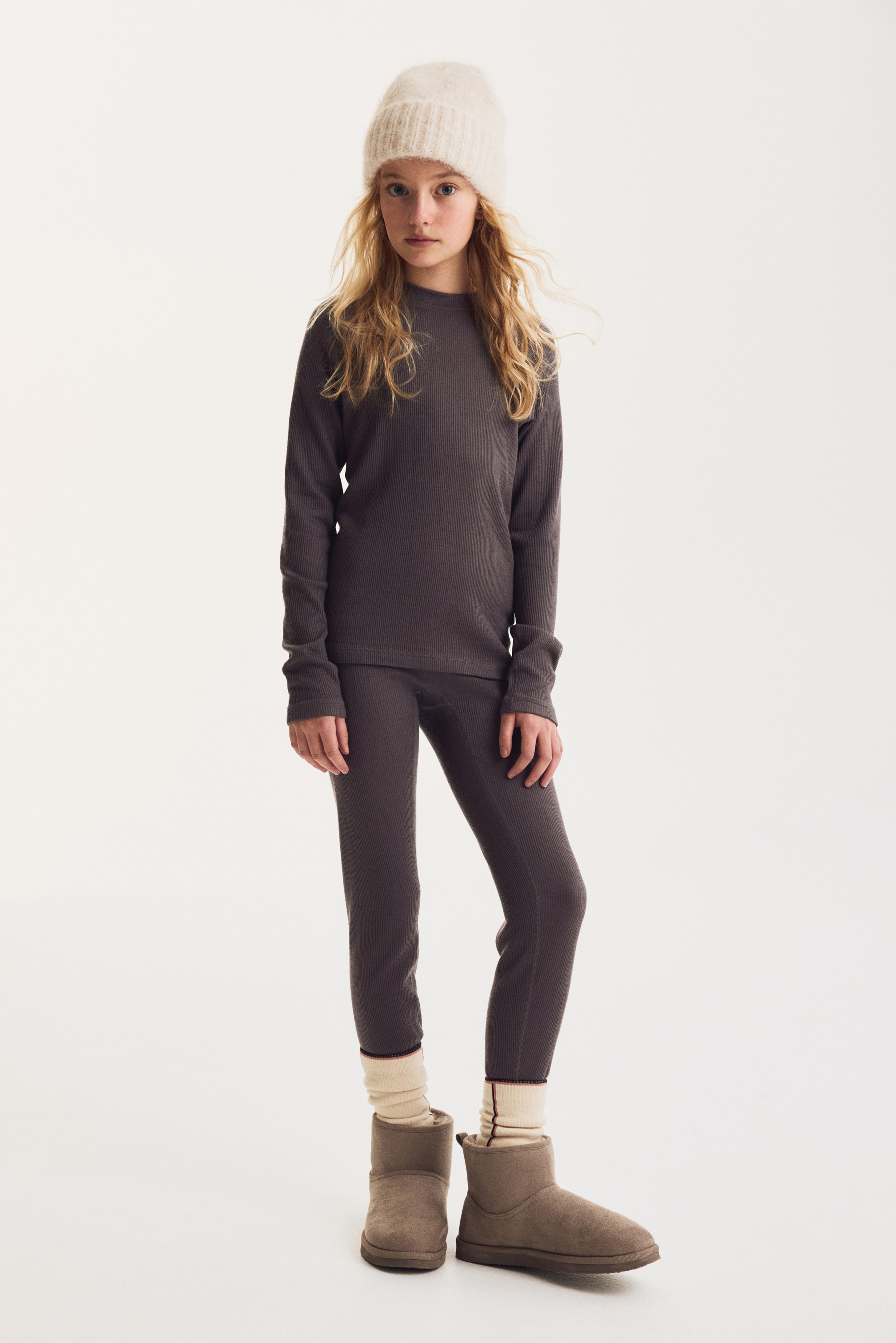 A two-piece ribbed knit lounge set in a dark purple-grey colour is hanging facing front, featuring a long-sleeve top with a crew neck and raglan sleeves, paired with matching slim-fit leggings.