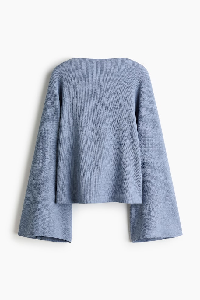 A light blue top is presented from the back, featuring a wide boat neckline, wide flared sleeves, and a subtle vertical crinkled texture. - 1