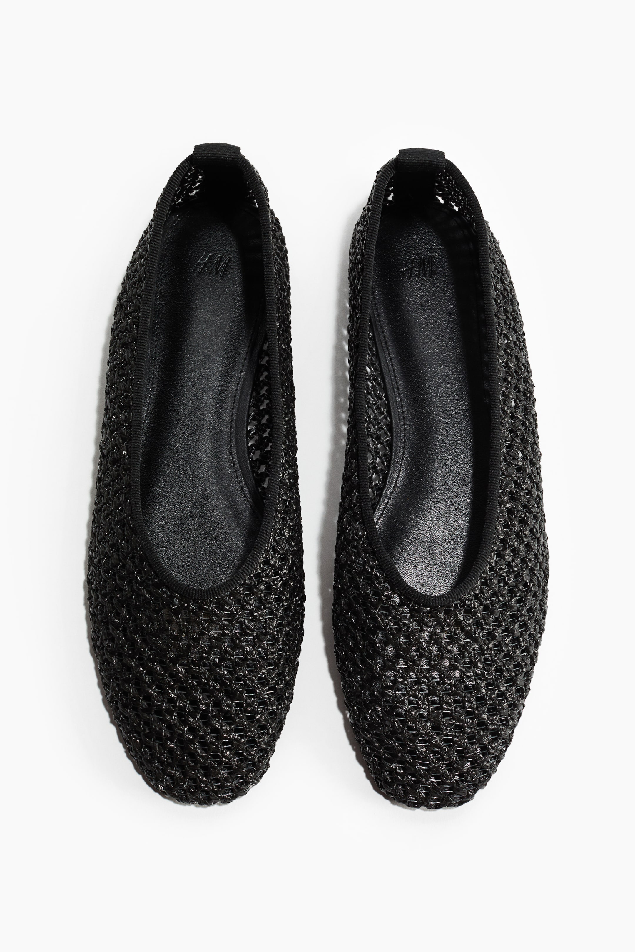 View larger image: Two black ballet flats lie side by side, showcasing a mesh-style woven texture across the uppers. They feature rounded toes and a thin black trim outlining the opening.