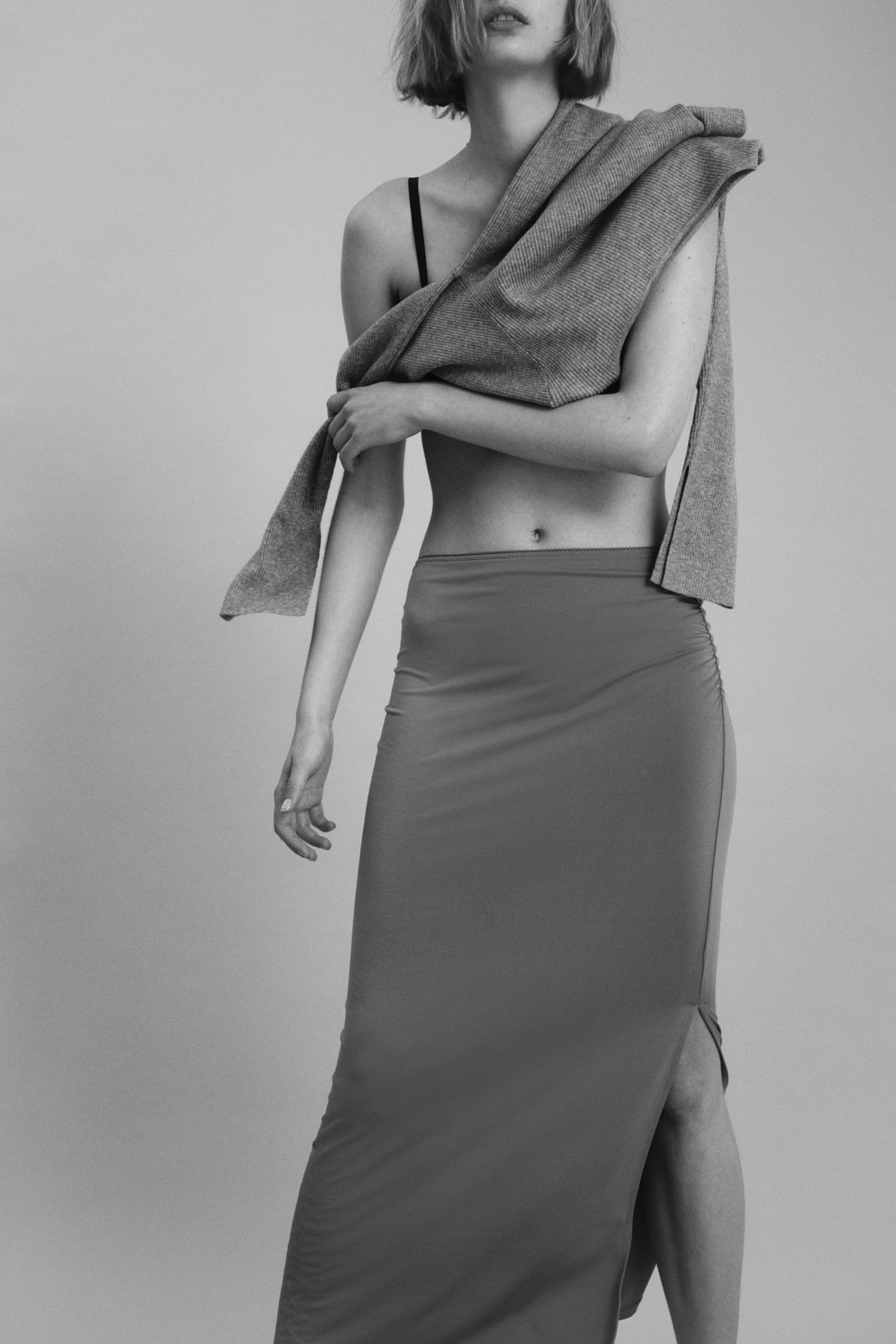 View larger image: Model memakai skirt midi jersey yang fit. Ia mempunyai pinggang tinggi dengan lipatan di sisi, menghasilkan efek drape lembut, dan potongan lurus dengan belahan tinggi di satu sisi.