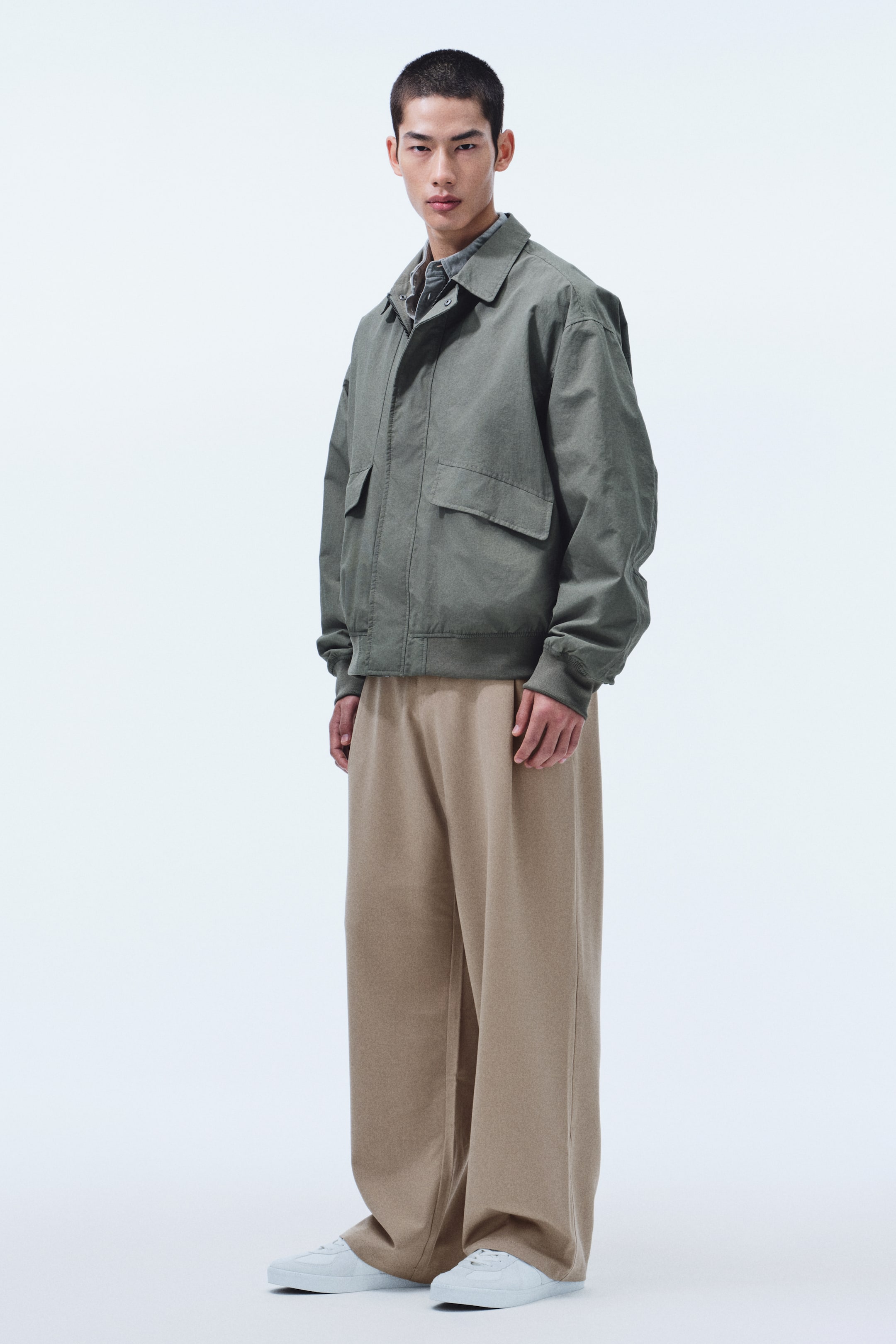 View larger image: Outfit shown from the front: an olive-green bomber jacket with a wide collar, two flap pockets, and ribbed cuffs and hem, worn over a patterned shirt, paired with wide-leg light brown pants and white low-top sneakers.