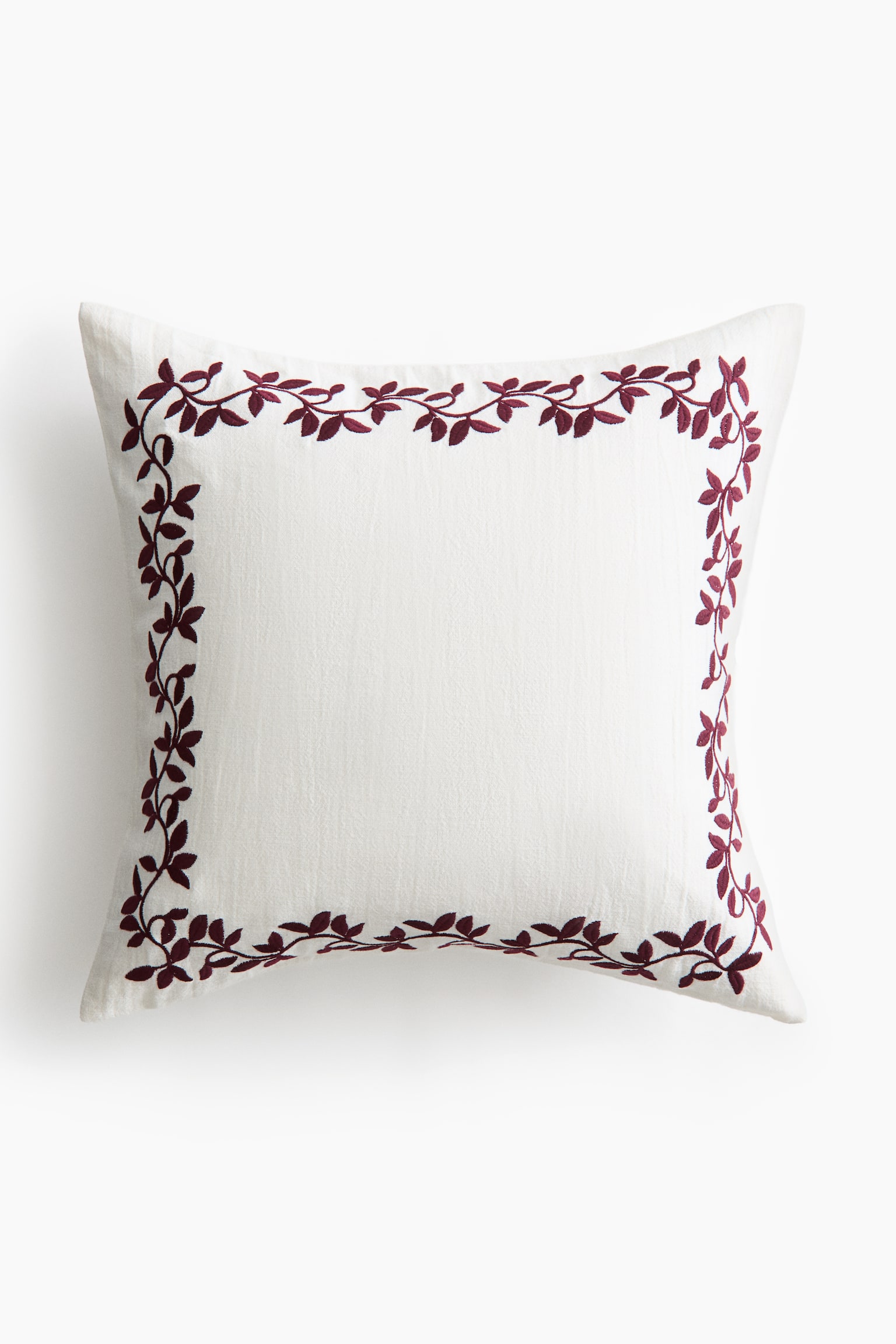 A square off-white cushion is facing front, featuring a dark burgundy embroidered vine-and-leaf border framing the outer edges of its textured slub fabric.