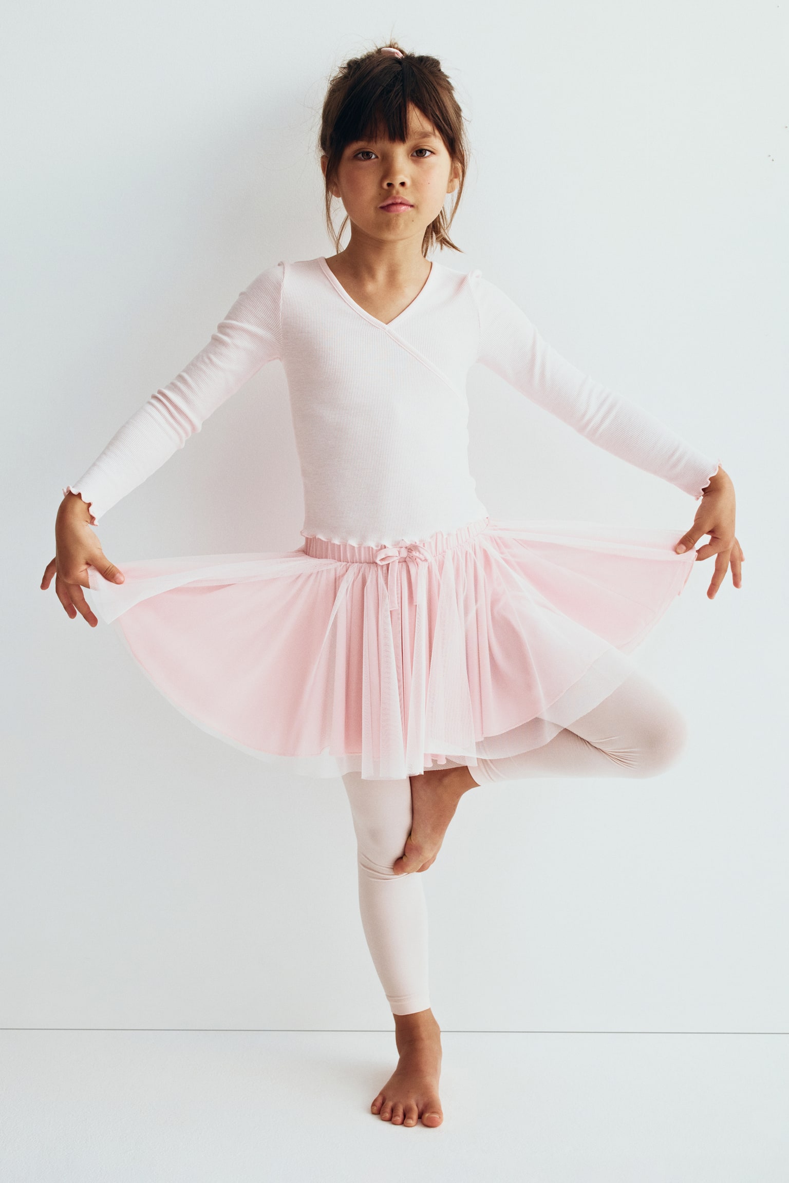 A pink tulle skirt with an elasticated waistband, adorned by a small decorative bow at the centre front, and several layers of gathered pink tulle forming a full silhouette. - 1
