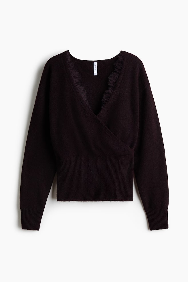 Un jersey de punto color ciruela oscuro visto de frente, con un diseÃ±o cruzado y un profundo escote en V rematado con un delicado ribete de encaje. El jersey presenta una textura suave, mangas largas con puÃ±os acanalados y una amplia cintura acanalada. - 1