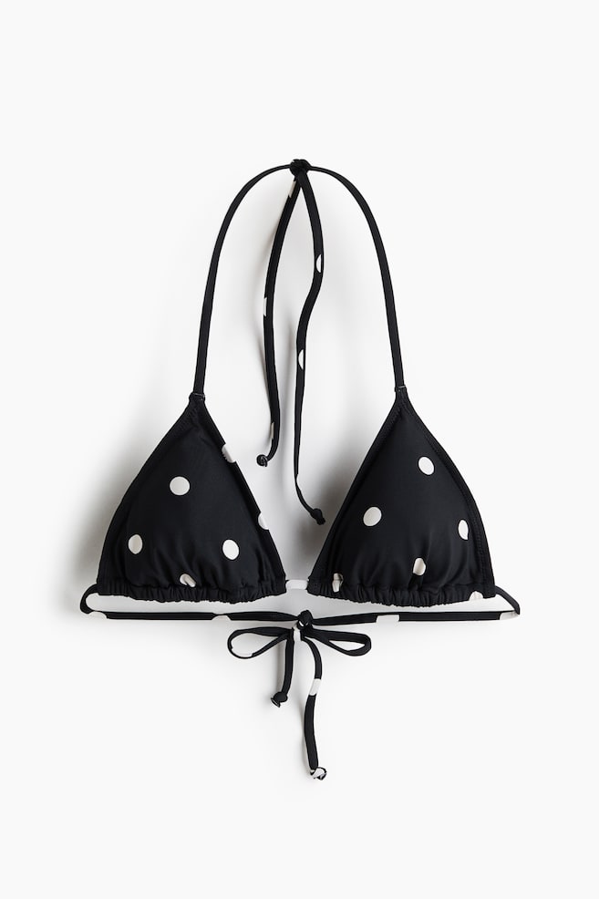 A black triangle bikini top with white polka dots is shown facing front, featuring two triangle cups and ties at the back and neck. - 1