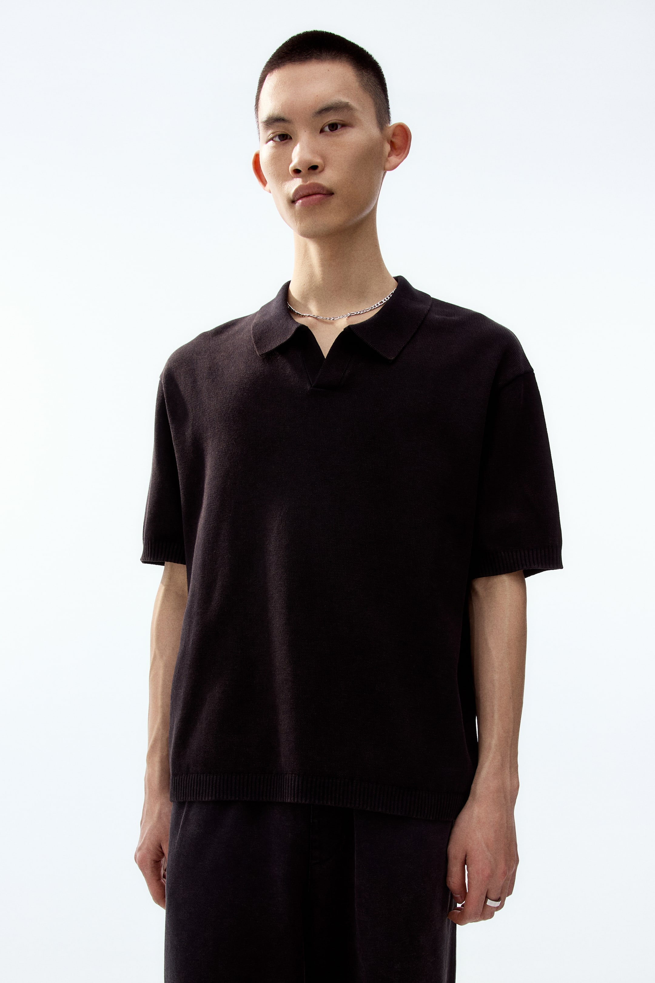 View larger image: A dark brown knit polo shirt features a spread collar and an open V-neck placket. It is designed with short sleeves, ribbed cuffs, and a ribbed hem for a relaxed fit.