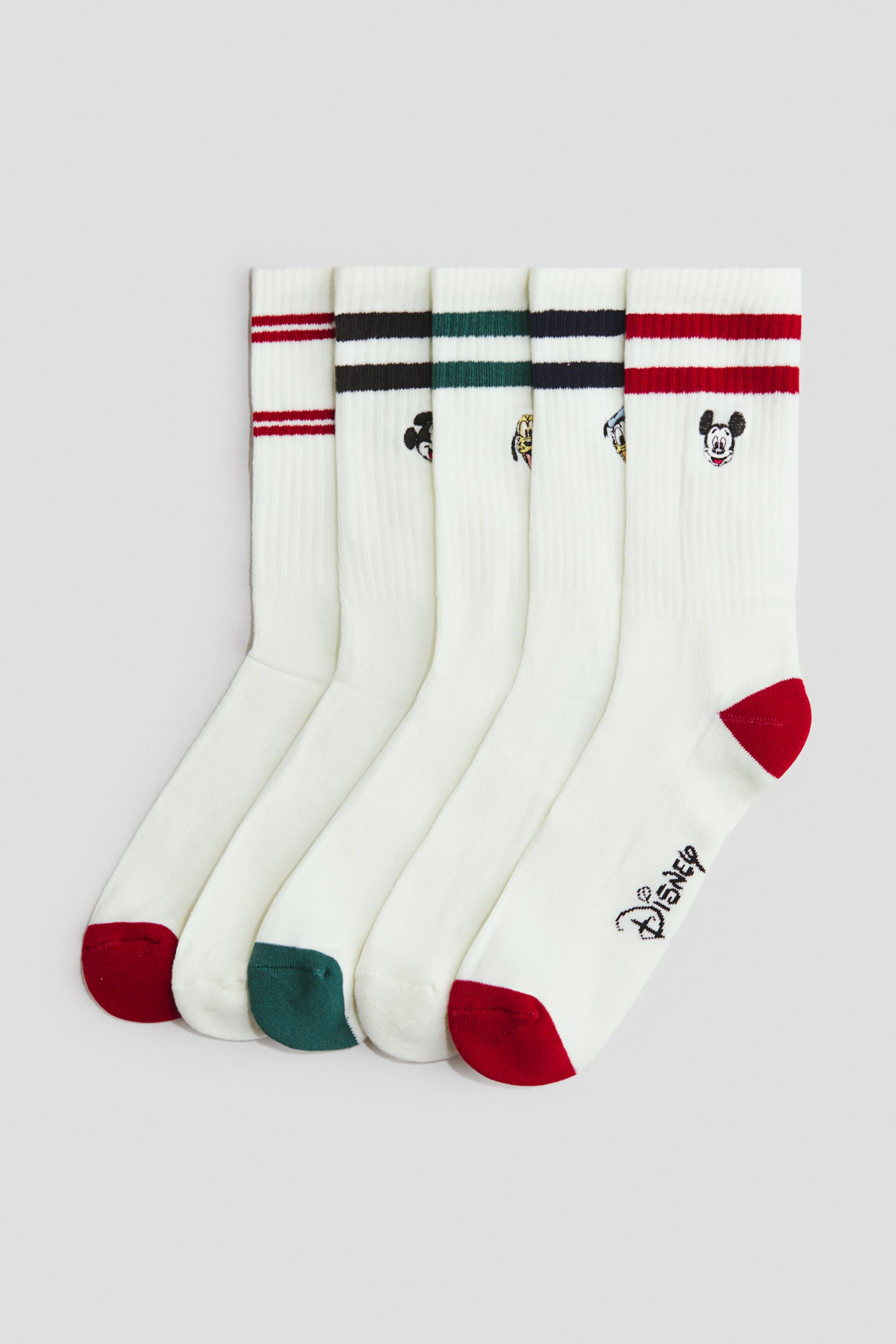 A set of five off-white, fine-knit crew socks is laid flat in an overlapping arrangement, showing their side profiles. The socks feature ribbed leg sections with elasticated cuffs, horizontal athletic stripes, small Disney character intarsia designs, and contrasting coloured heels and toes.