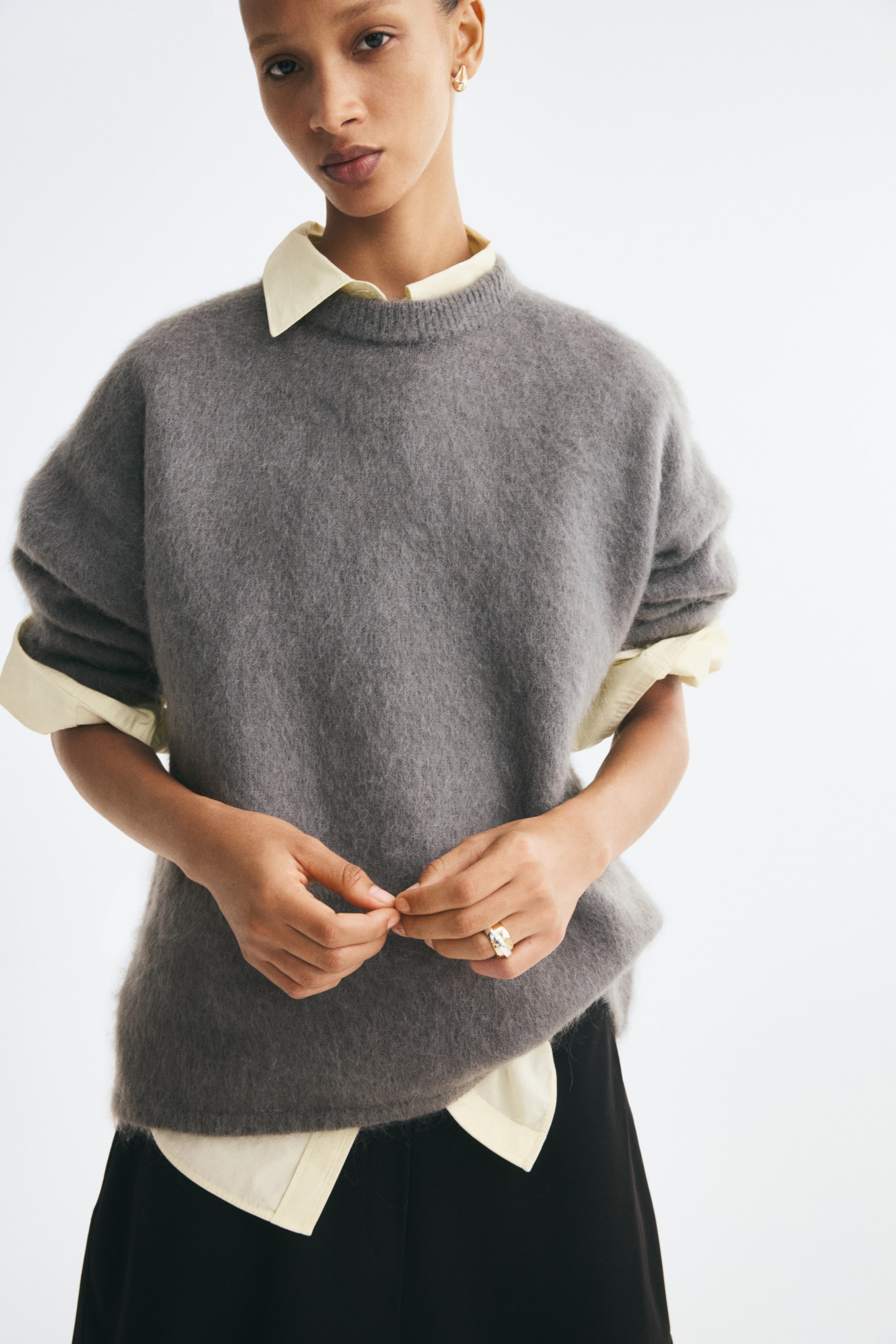 Voir une image plus grande: Un chandail en tricot gris surdimensionné est présenté de face, mettant en valeur une texture duveteuse, un col ras du cou côtelé et des épaules tombantes. Le chandail est superposé à une chemise à col jaune pâle, dont le col et l’ourlet dépassent pour souligner la coupe décontractée et ample.