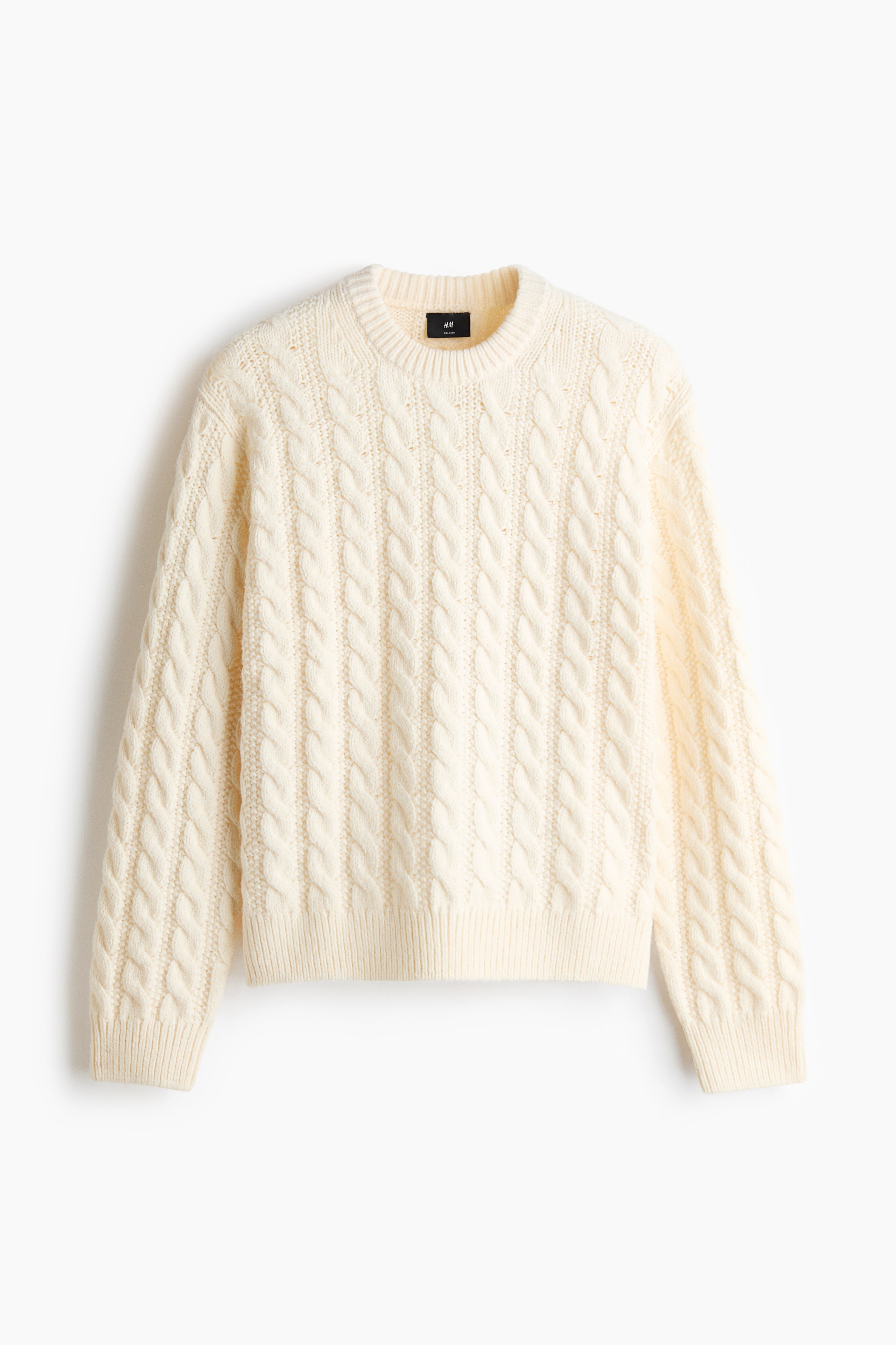 Ver imagen más grande: Se muestra un jersey de punto trenzado de color crema desde un ángulo frontal y plano, con cuello redondo rematado en rib y un corte relajado. Los patrones verticales de punto trenzado recorren el cuerpo y las mangas largas, que terminan en puños acanalados y un dobladillo acanalado a juego.