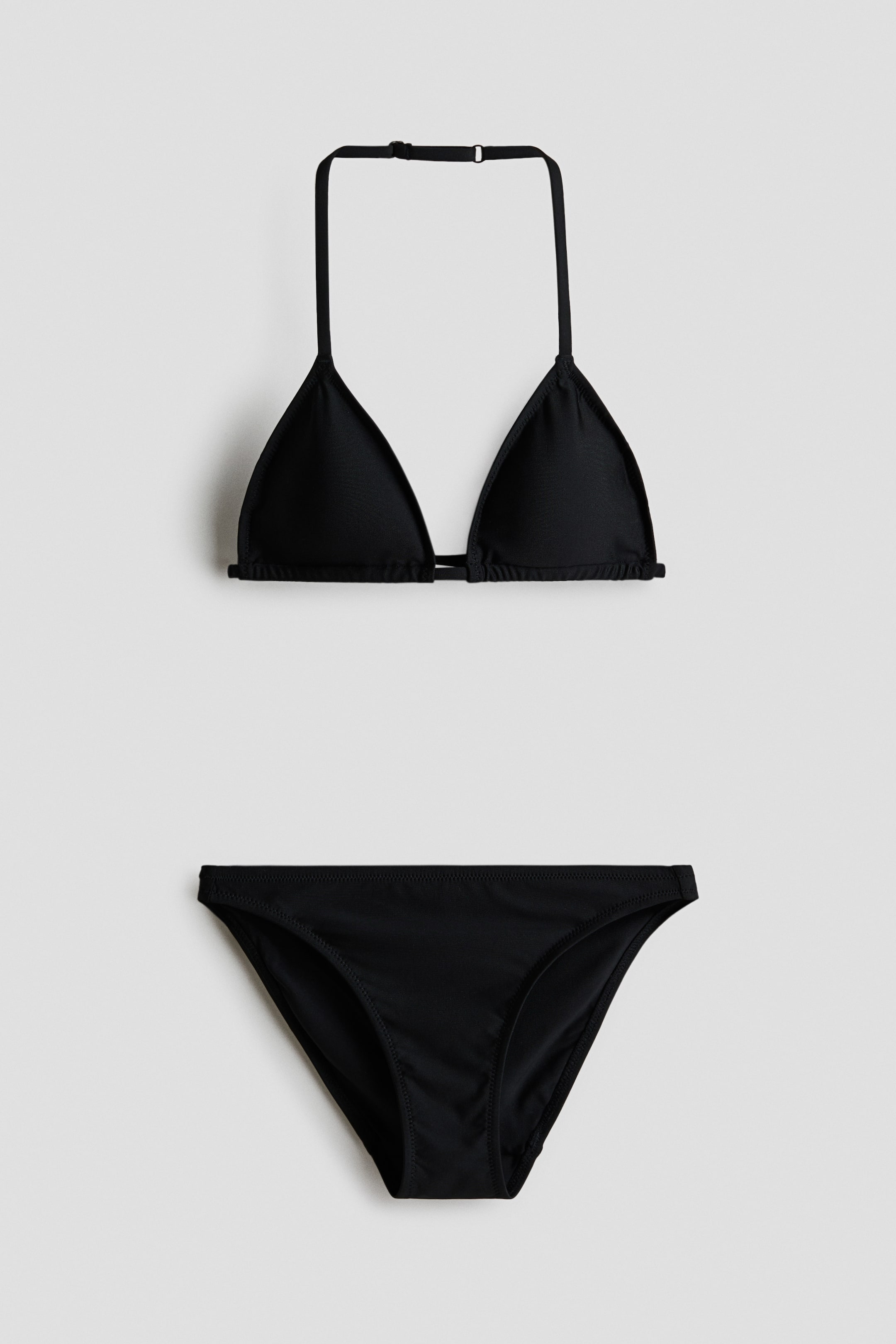 Nagyobb kép megtekintése: Egy teljesen bélelt fekete bikini szett kerül bemutatásra, amely háromszög alakú bikini felsőt és hozzá illő alsót tartalmaz. A felső kivehető betétekkel, állítható nyakpánttal és műanyag kapoccsal a háton van kialakítva.