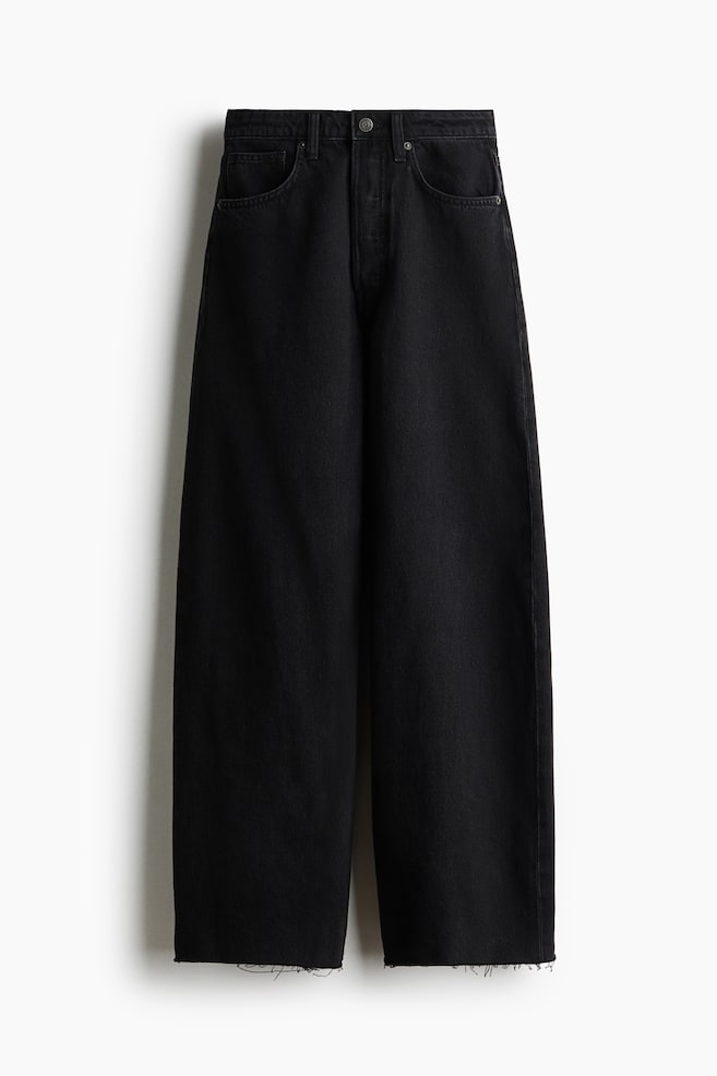 Een paar zwarte denim jeans van katoen wordt van voren getoond, met een hoge taille, een knoopsluiting en klassieke five-pocket-styling. De jeans is ontworpen met een volumineuze, gebogen pijp die toeloopt naar gerafelde, onafgewerkte boorden. - 1