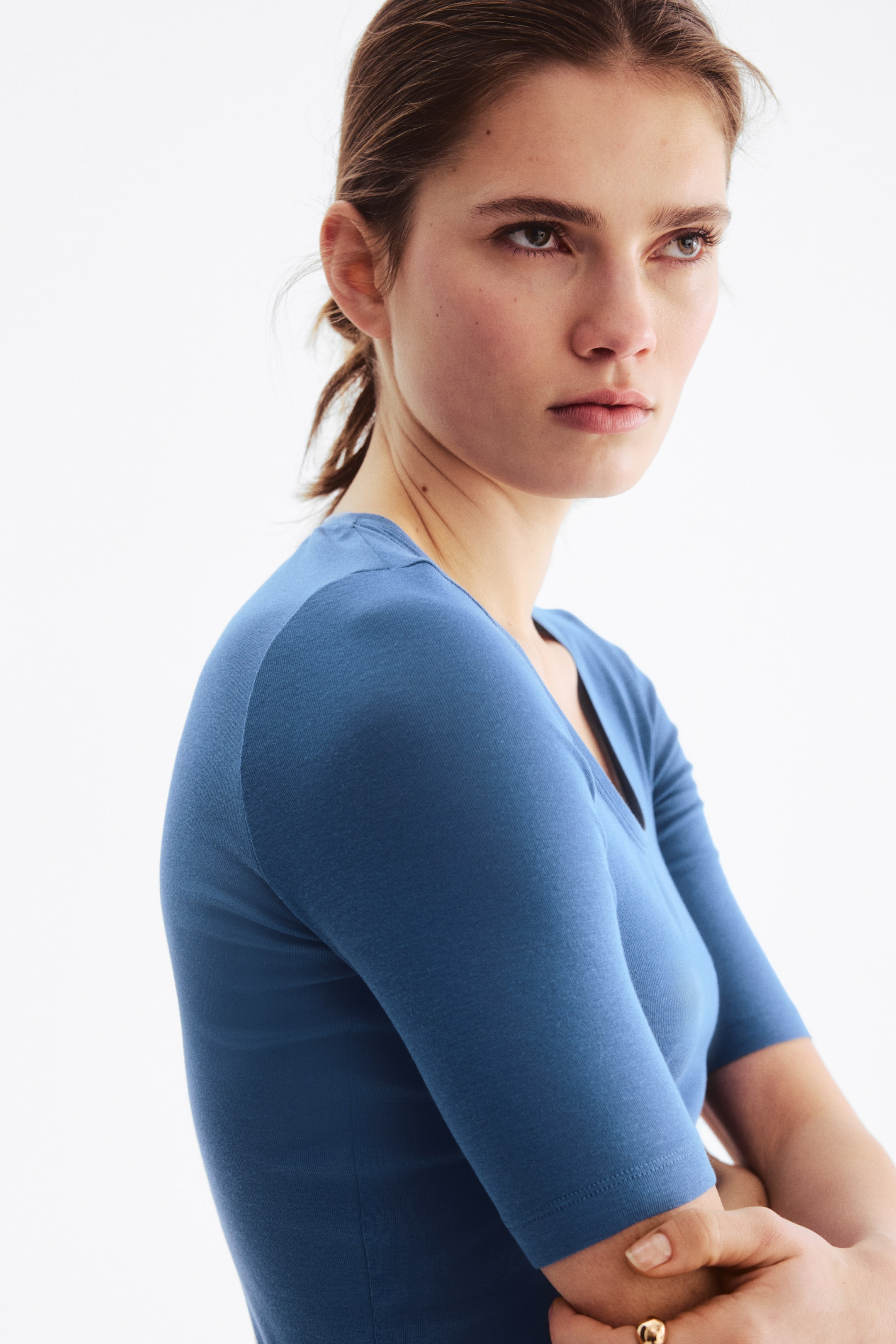View larger image: A blue top featuring a V-neckline and elbow-length sleeves, showcasing a fitted silhouette from a side angle.