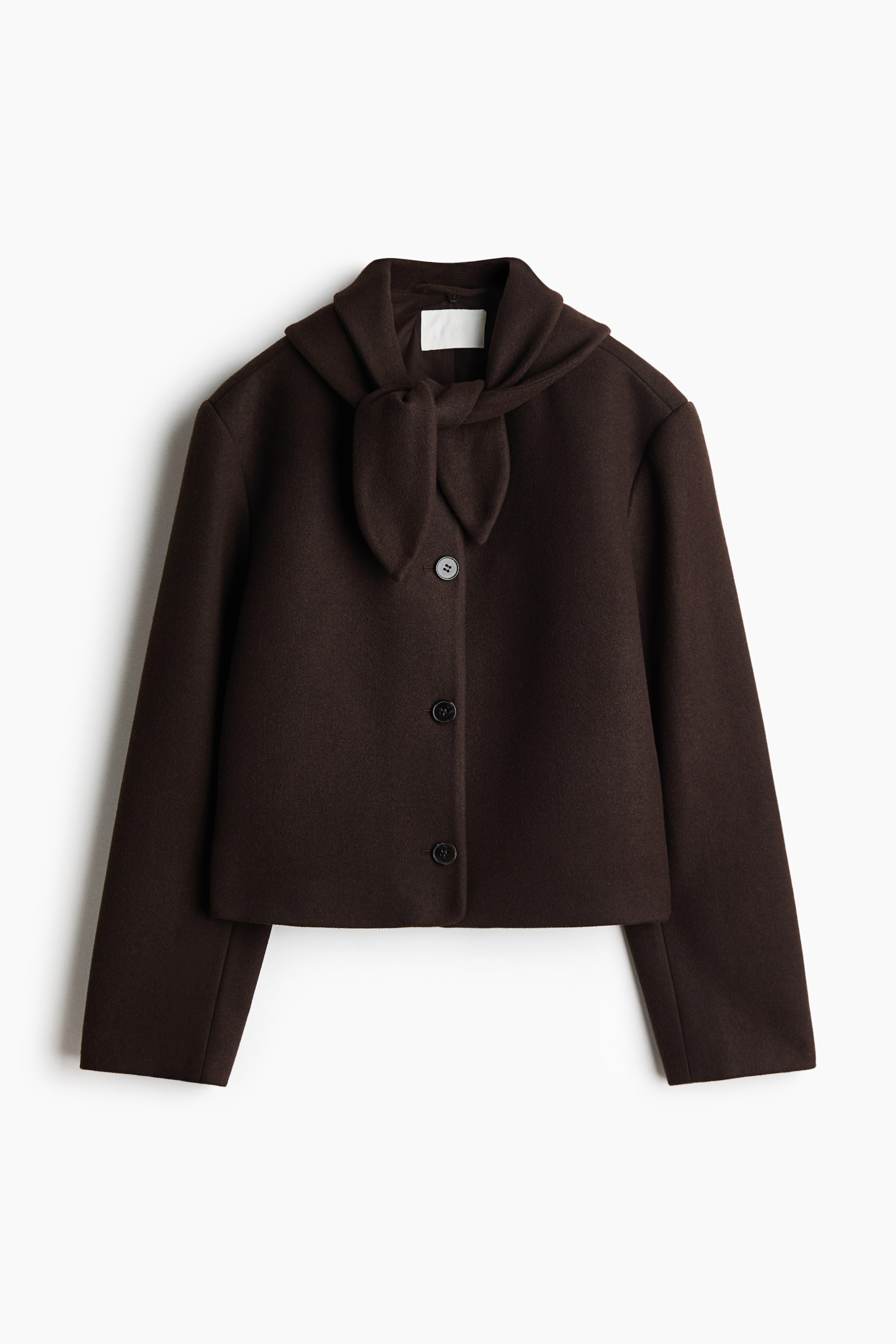 View larger image: A dark brown cropped jacket is shown from the front, featuring an integrated tie-neck collar knotted at the front. Three dark buttons fasten the front, and long sleeves are visible.