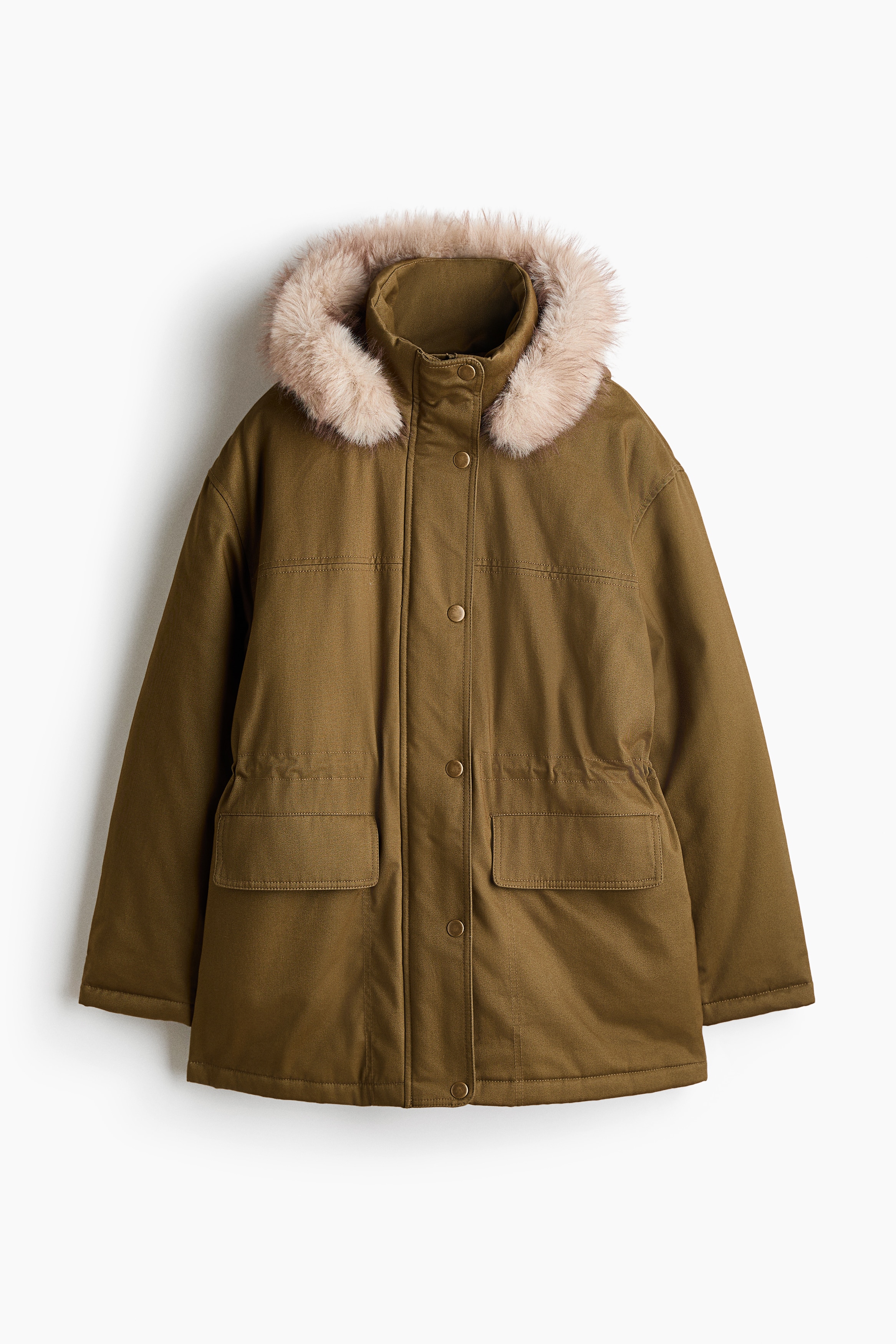 An oversized, lightly padded olive green parka is worn open by the model, featuring a hood with fluffy faux-fur trim and front flap pockets. The parka is layered over a white graphic sweatshirt and wide-leg, pinstriped grey trousers.