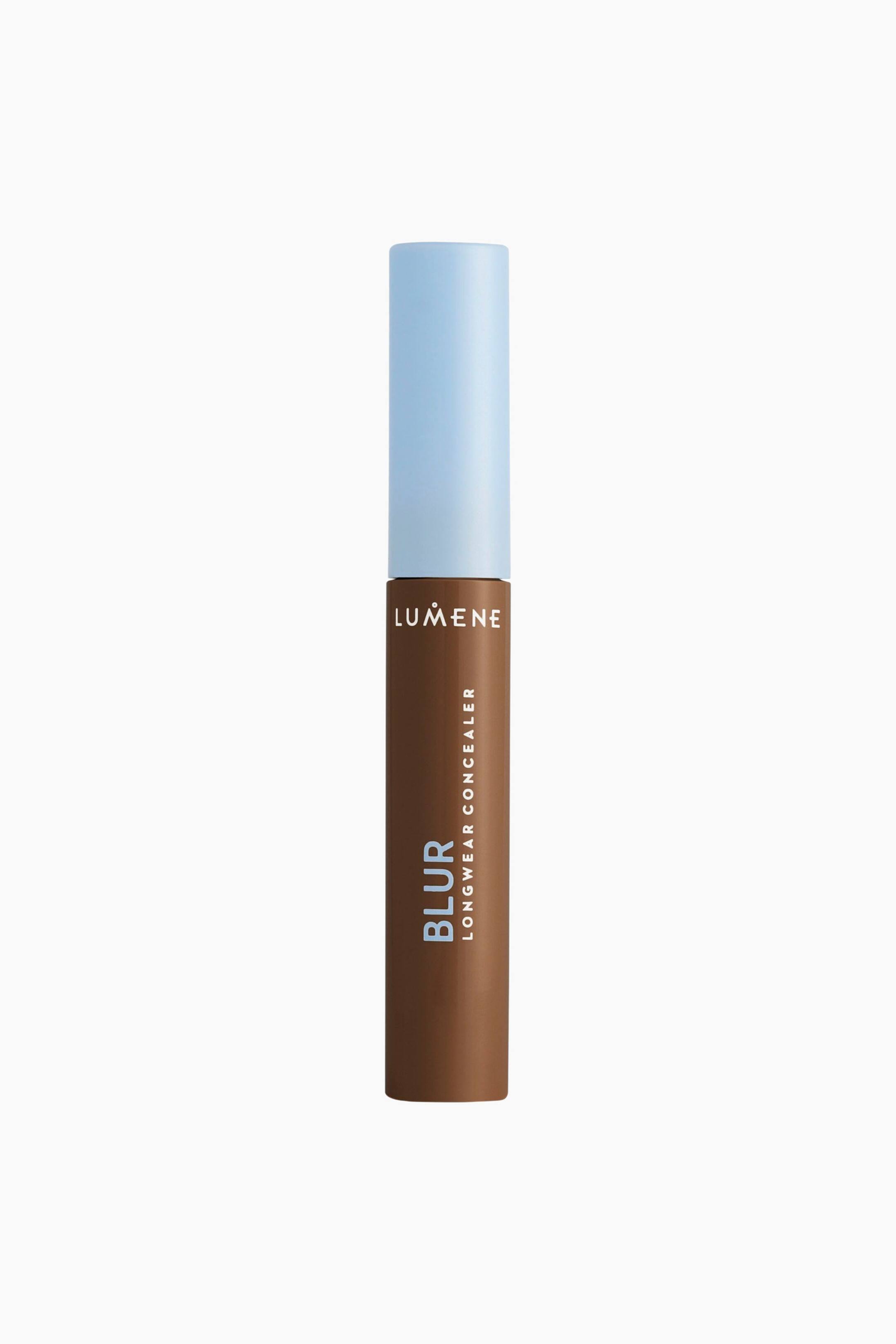 Visa större bild: En tub med Lumene Blur Longwear Concealer står upprätt och visar en mörkbrun cylindrisk behållare med ett matt ljusblått lock. Behållaren har den vita logotypen ”LUMENE” nära toppen, med ”BLUR” i stora ljusblå lodräta bokstäver och ”LONGWEAR CONCEALER” i mindre vita lodräta bokstäver längs sidan.