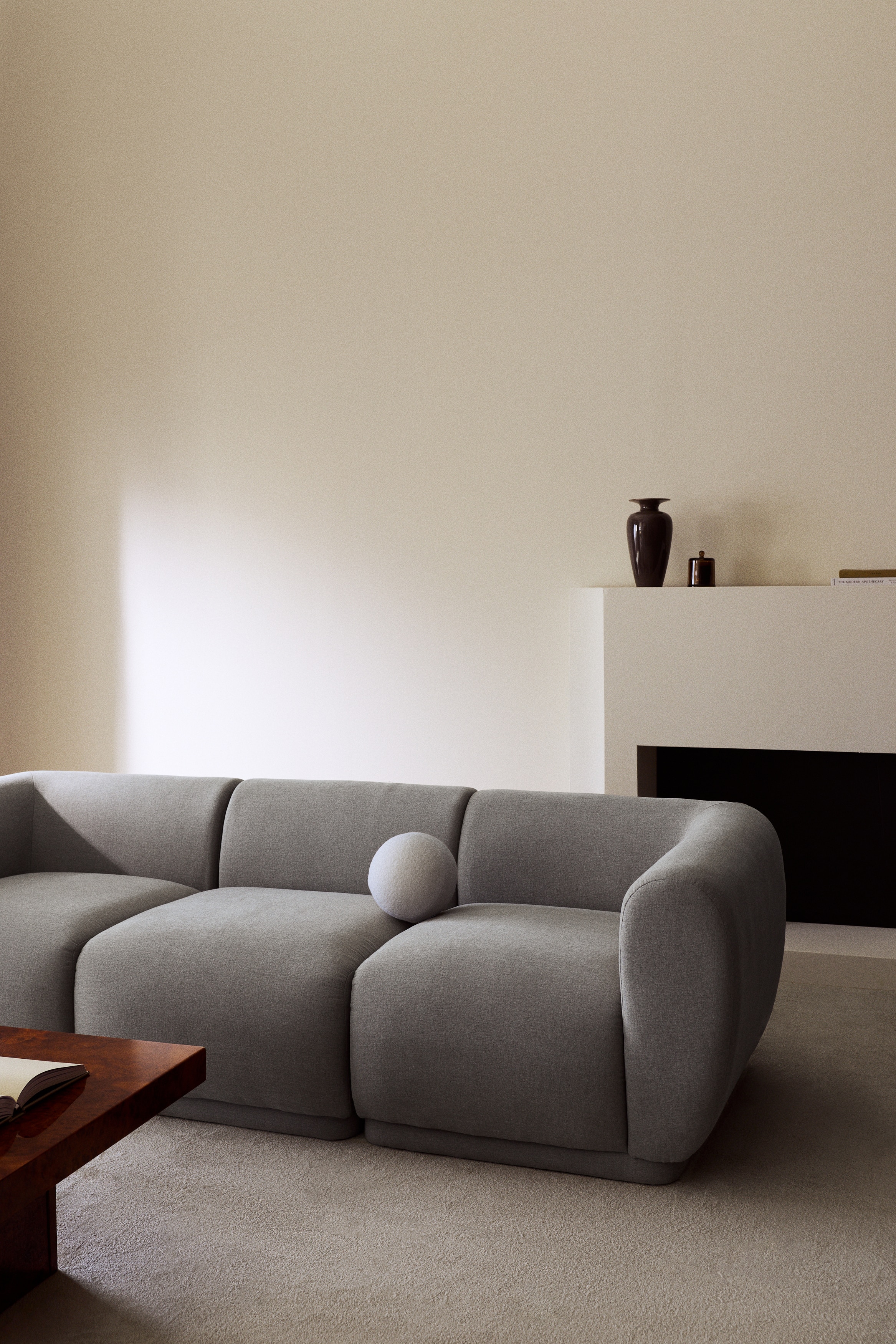 Un canapÃ© trois places recouvert dâun tissu texturÃ© gris clair est orientÃ© vers lâavant, avec un design bas et trois coussins dâassise modulaires bien rembourrÃ©s. Le canapÃ© met en valeur de larges accoudoirs arrondis qui se fondent harmonieusement dans le dossier bas, lâensemble reposant sur une base basse en retrait.